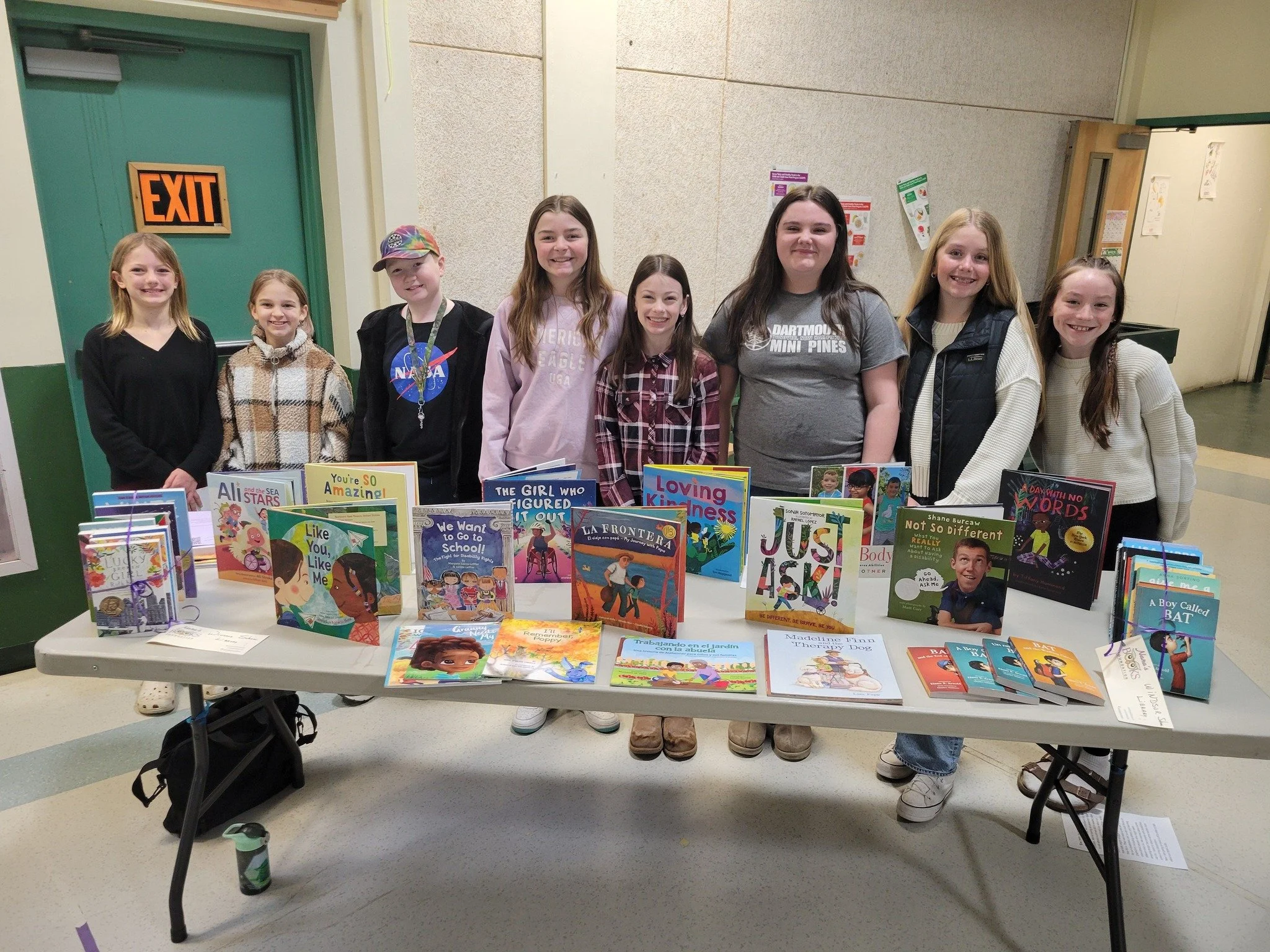Older students standing behind a table displaying a collection of children’s and young adult books.