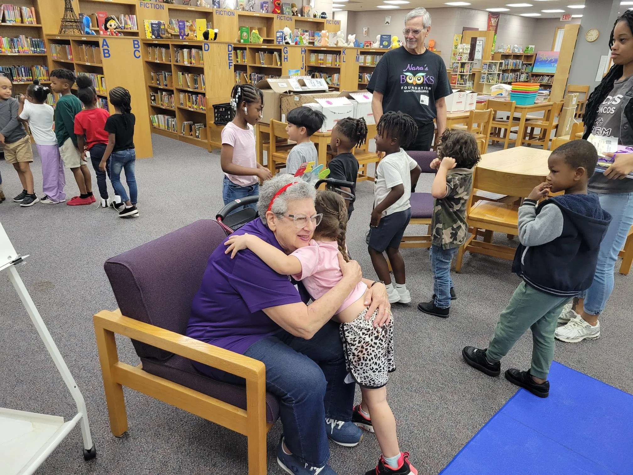 Child hugs a Nana’s Books Foundation volunteer during a book distribution at a school library.