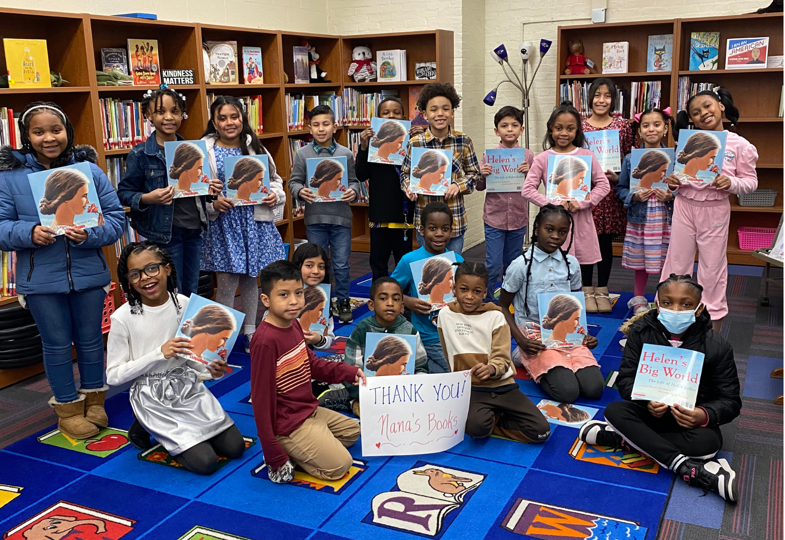 Students at Owings Mills Elementary hold donated books around a handwritten “Thank You! Nana’s Books” sign in their school library.