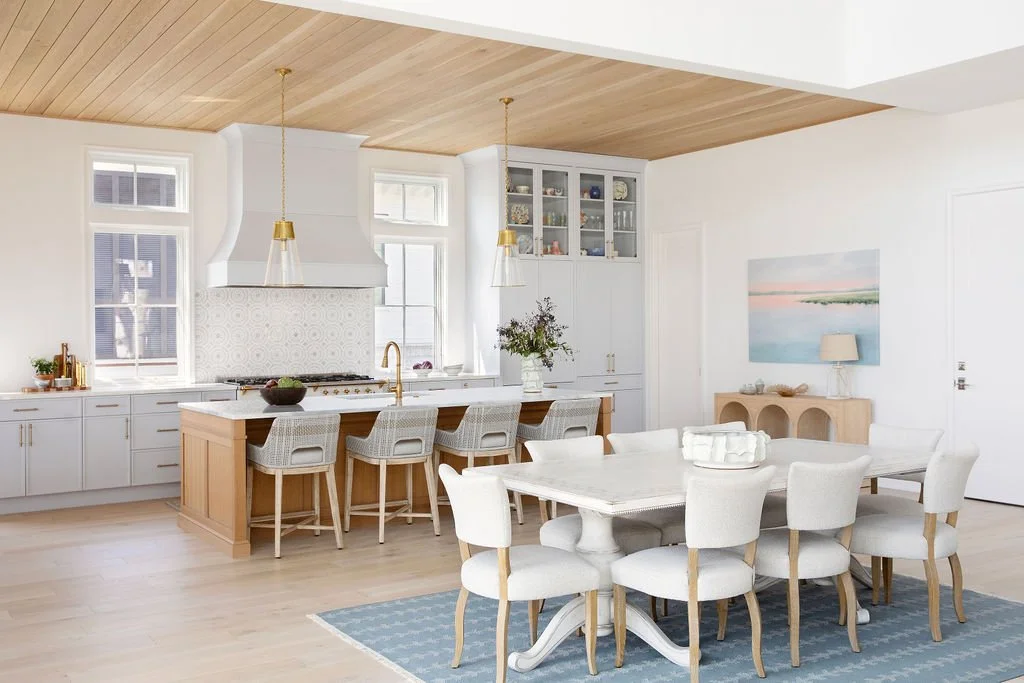 Open kitchen and dining area with white cabinets, wooden island, and light-colored furniture.