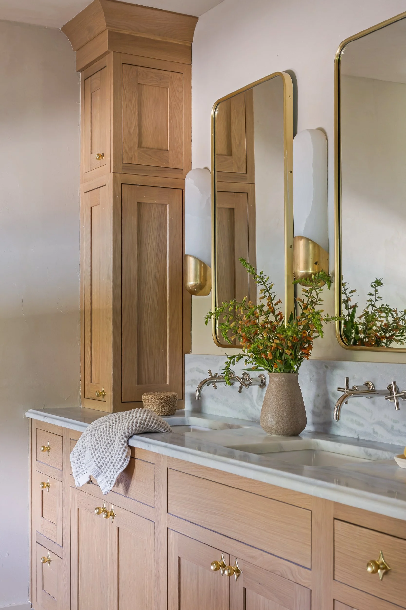 Bathroom vanity with wooden cabinets, a marble countertop, a potted plant, a towel, and framed mirrors