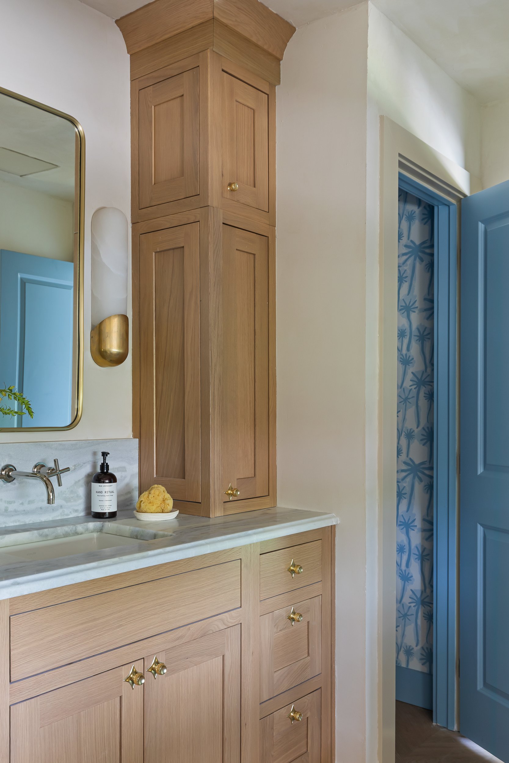 A bathroom corner with a wooden cabinet above a marble countertop by Charleston interior stylist Ellen Casey