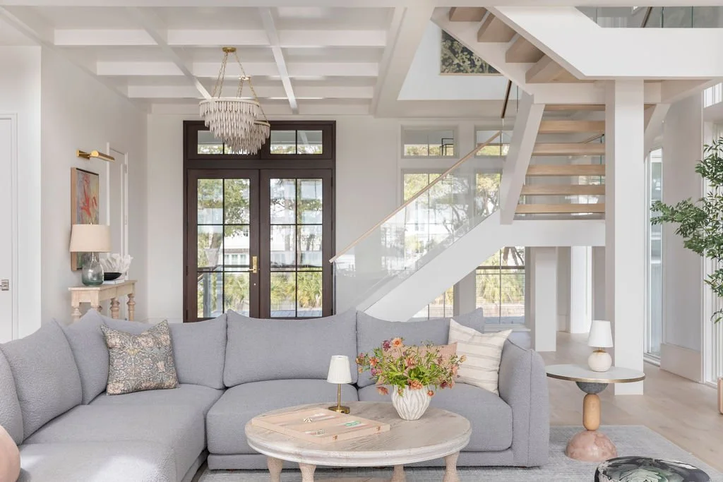 Modern living room with a gray sectional sofa, coffee table, and staircase near a glass door.
