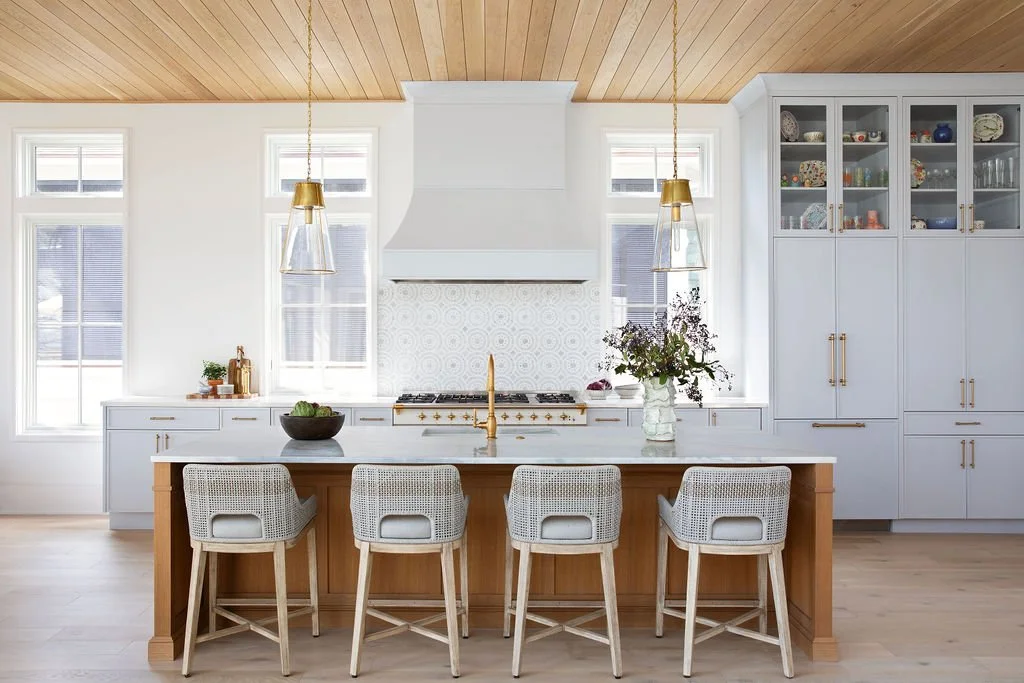 Bright kitchen with white cabinets, a large island with a wooden base, four bar stools, a gold faucet, and pendant lights by Charleston interior stylist Ellen Casey
