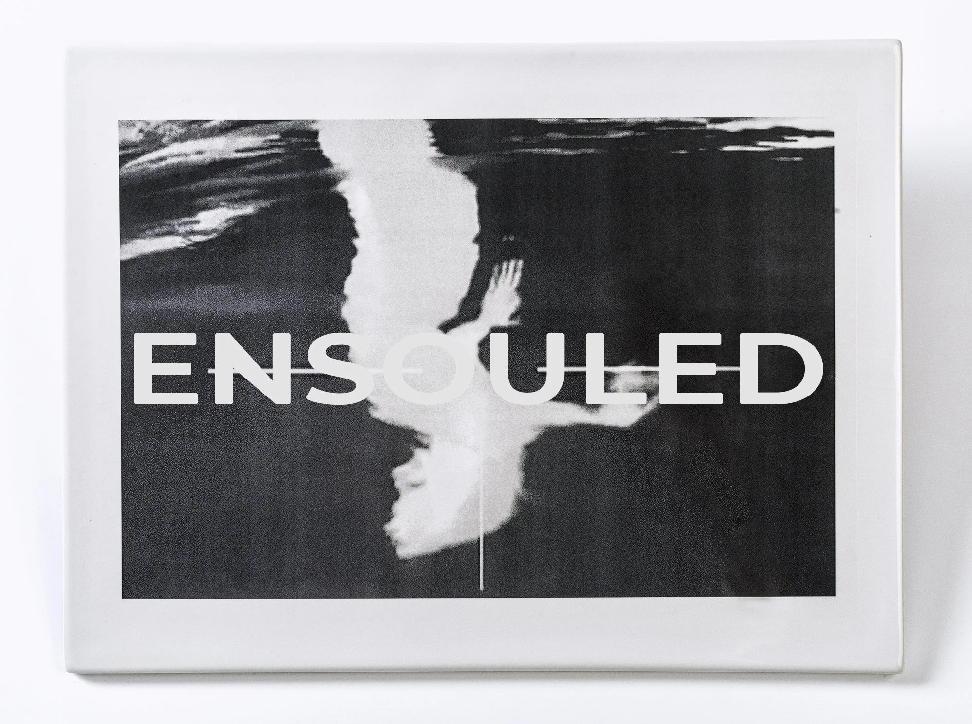 'Shadow self (Ensouled)', 10.25 x 14 x .30 inches, vitreous porcelain, infrared video still as photo decal, cork, 2025, unique.

Tile made at Arts/Industry, a residency program of the JMKAC, in Pottery Division, Sheboygan, WI.