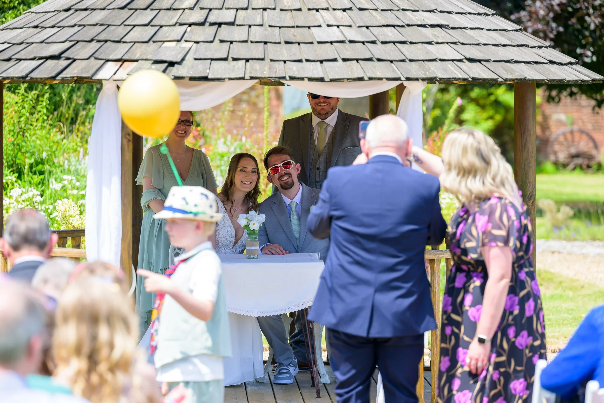 A bride and groom posing for the camera while sat under a hut