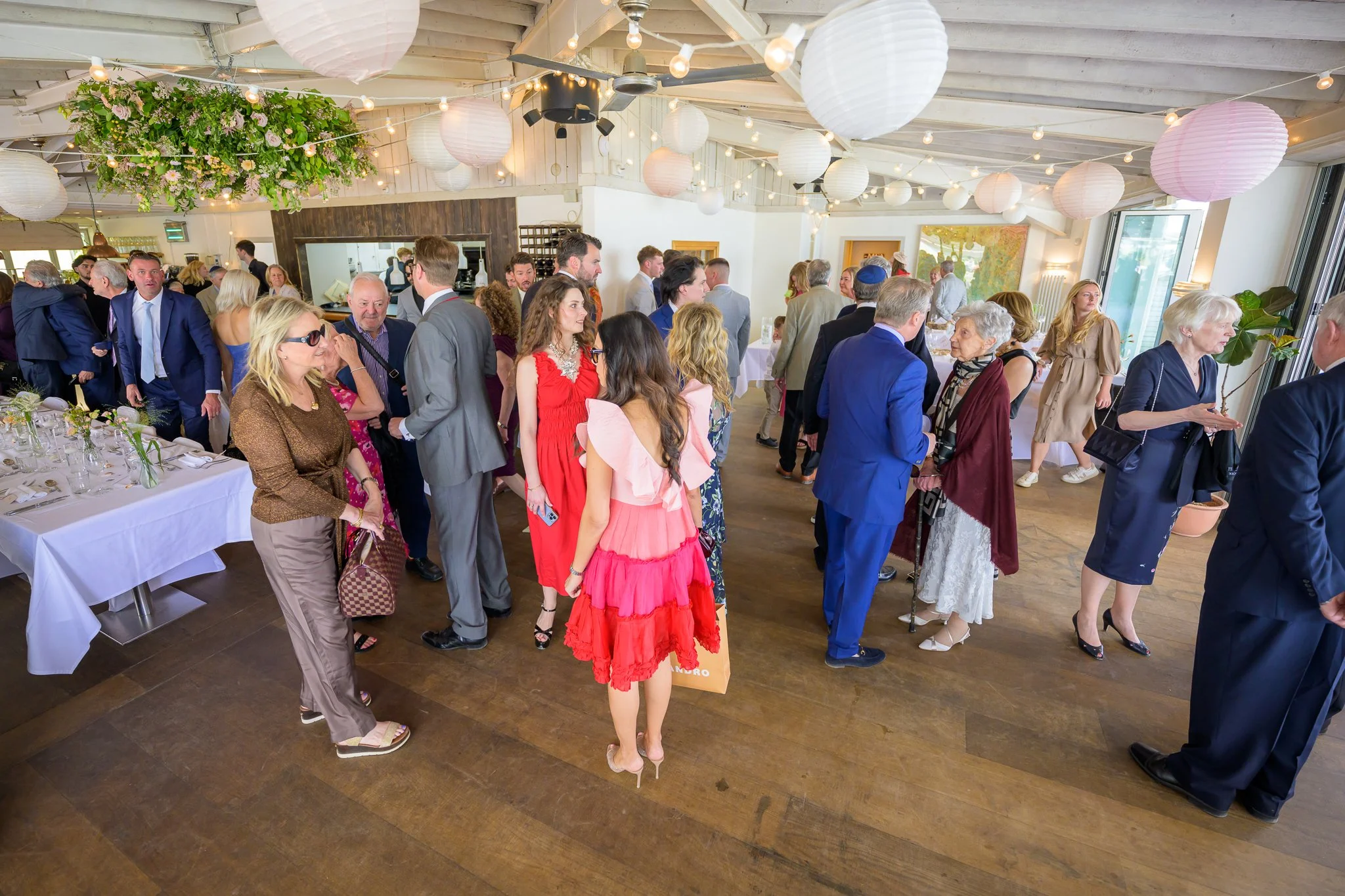 Wedding guests standing around on the dance floor of a wedding venue, with decorations above them