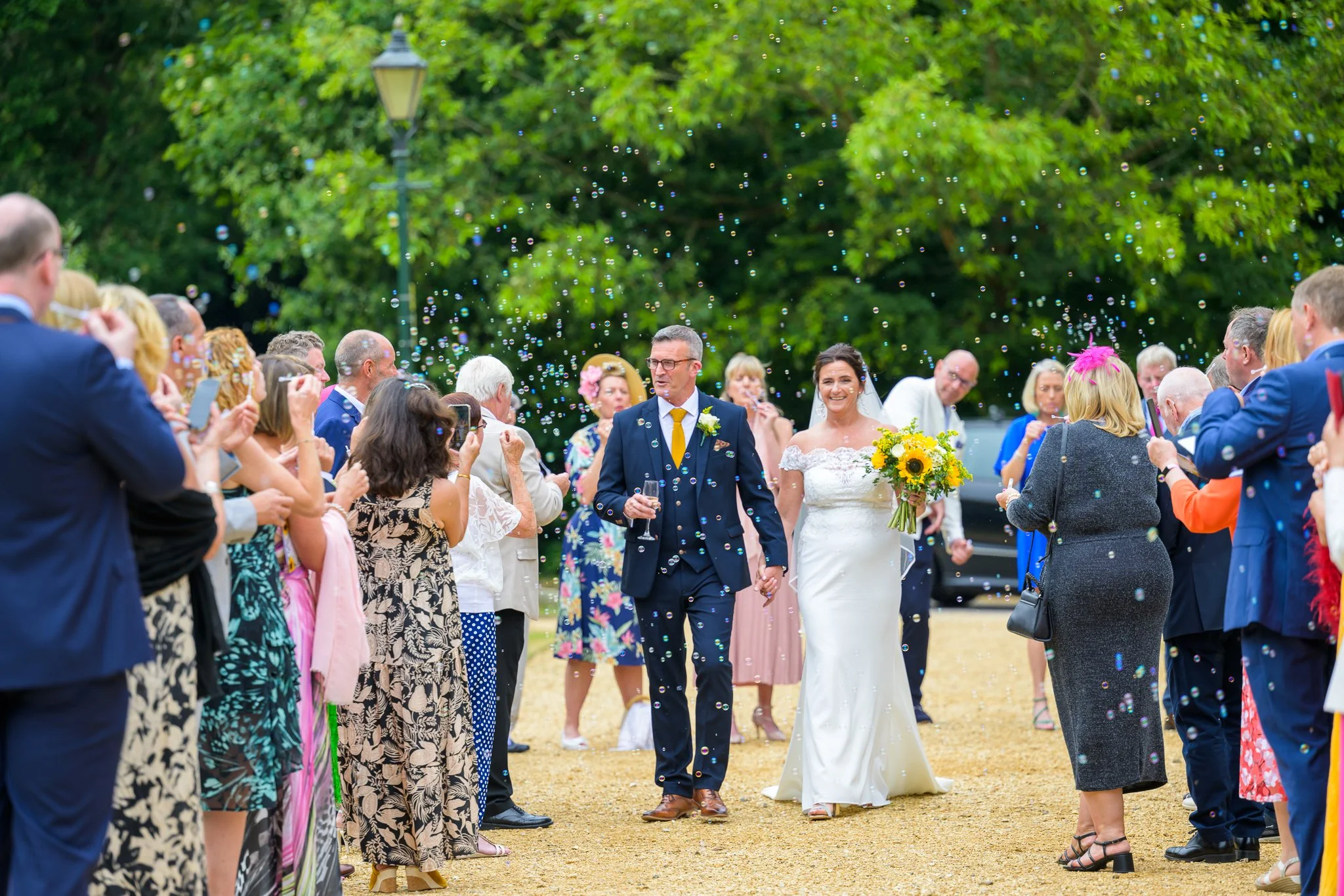 Bride and groom walking through the aisle towards their wedding venue with their wedding guests surrounding them