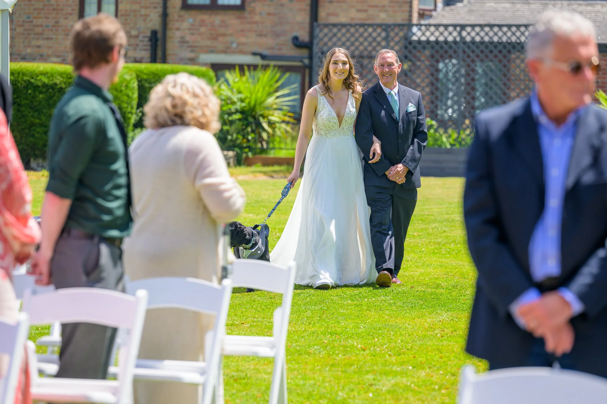A bride, her father, and her dog about to walk through the aisle, with the wedding guests standing and waiting for them to come through