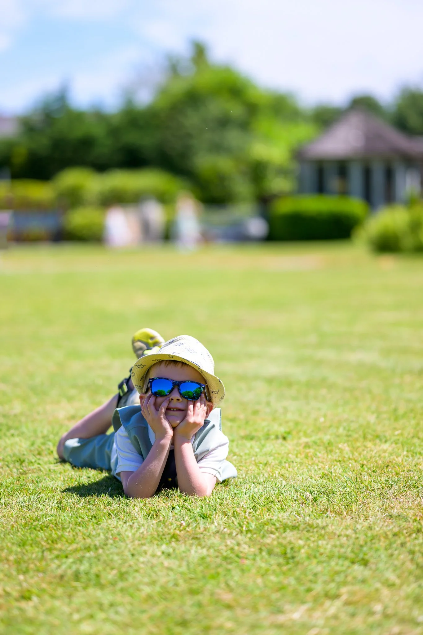 A child laying down, holding his head up on a field, posing for a camera
