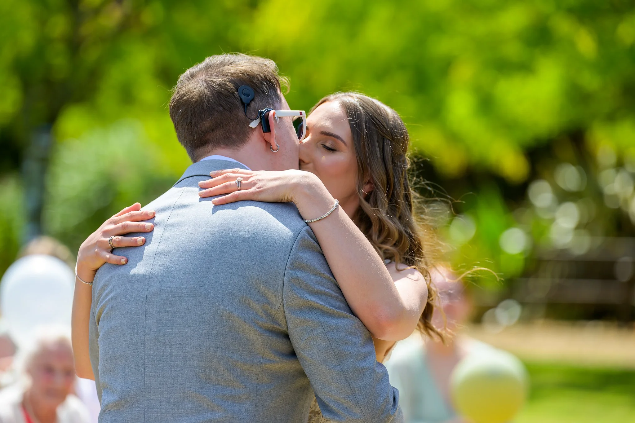 A bride anf groom hugging and kissing outside with a blurry and green background