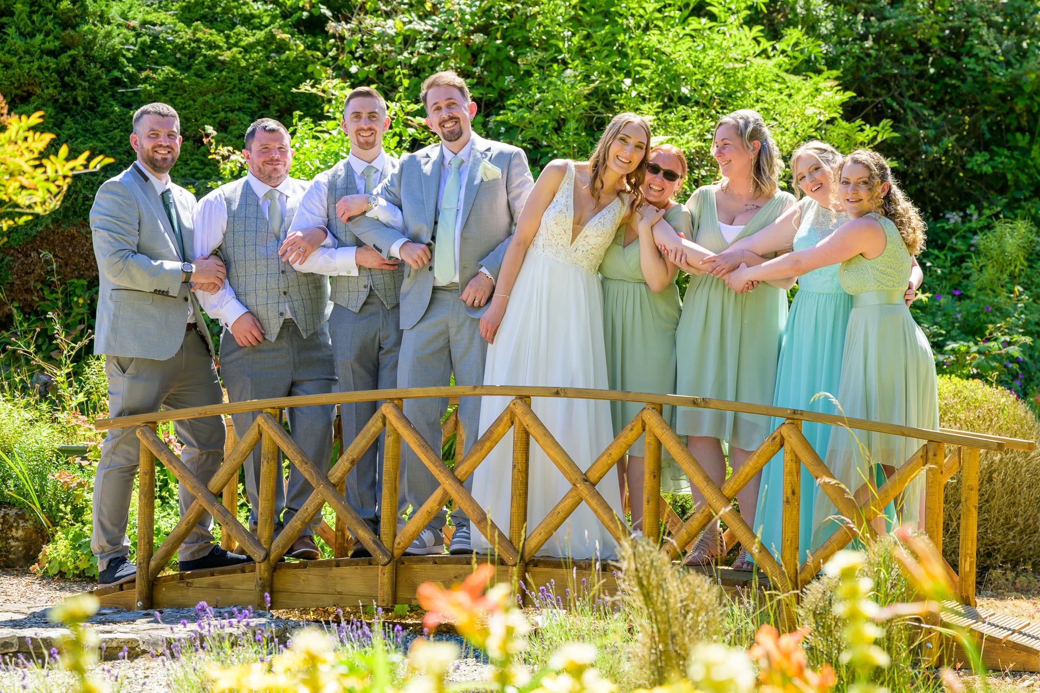 The groom and his best Men, and a bride and her bridesmaids posing for the camera while stood on a bridge