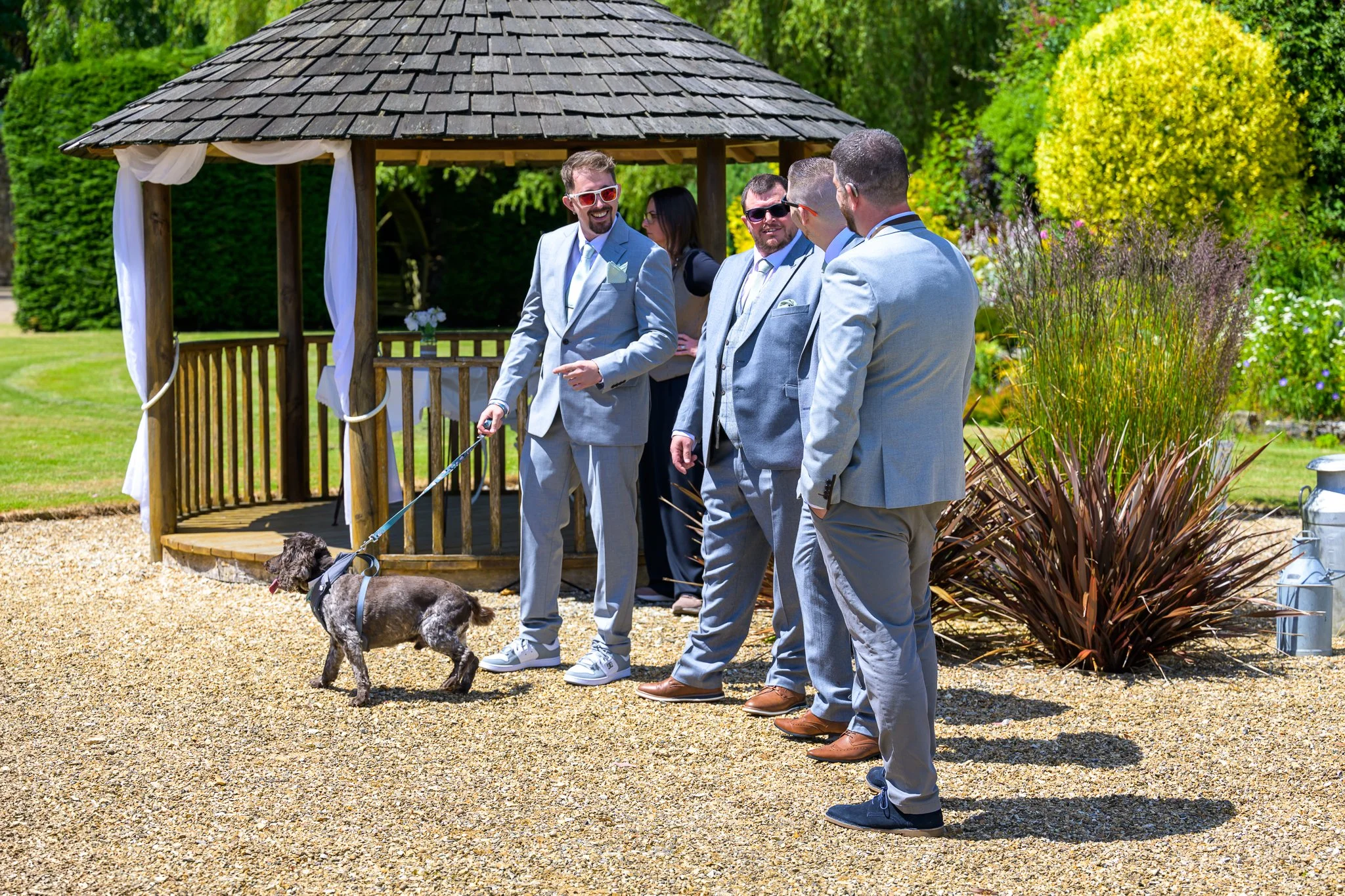 Groom and his bestmen having a conversation next to a hut, with bushes and a dog next to them