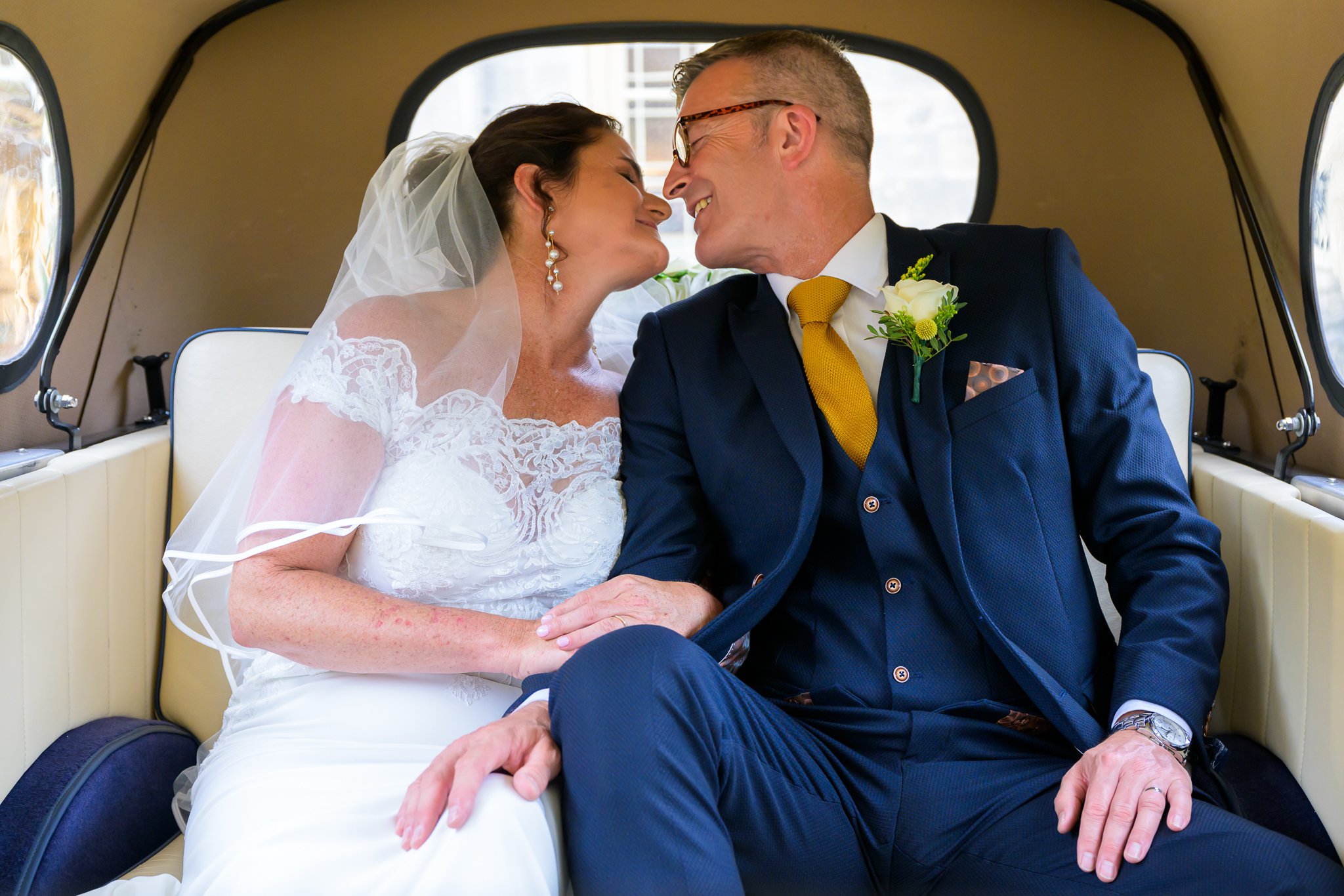Bride and groom sat in their wedding car kissing