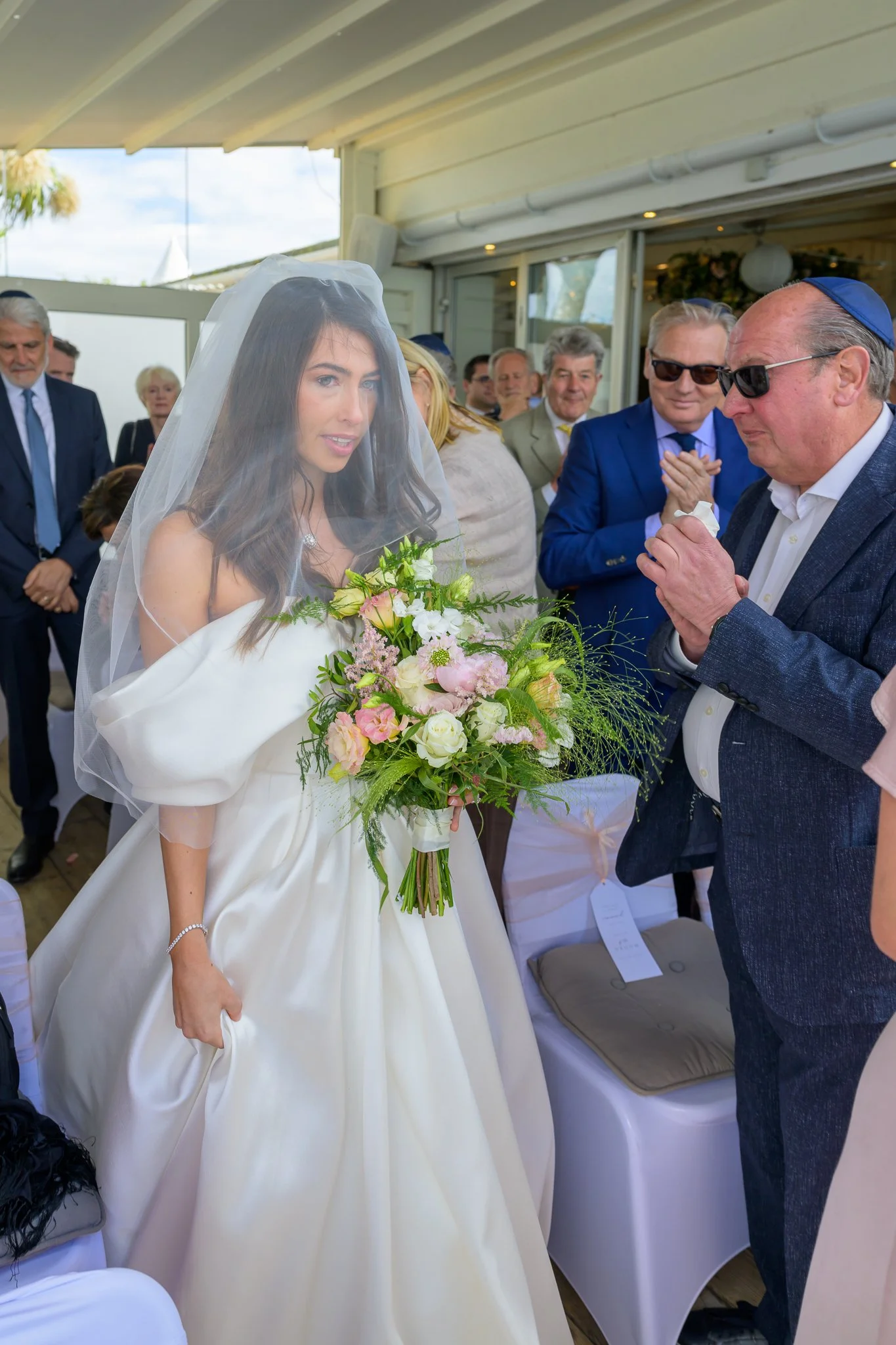 Bride holding flowers with her wedding guests surrounding her