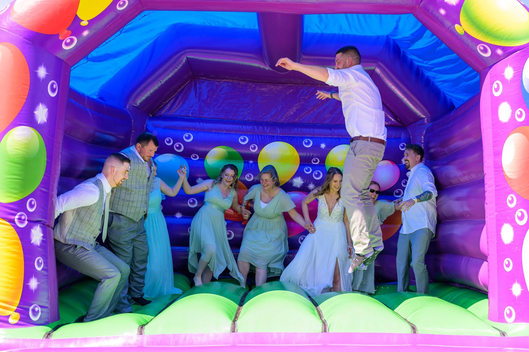 A bride, groom, and wedding guests having fun in a bouncy castle