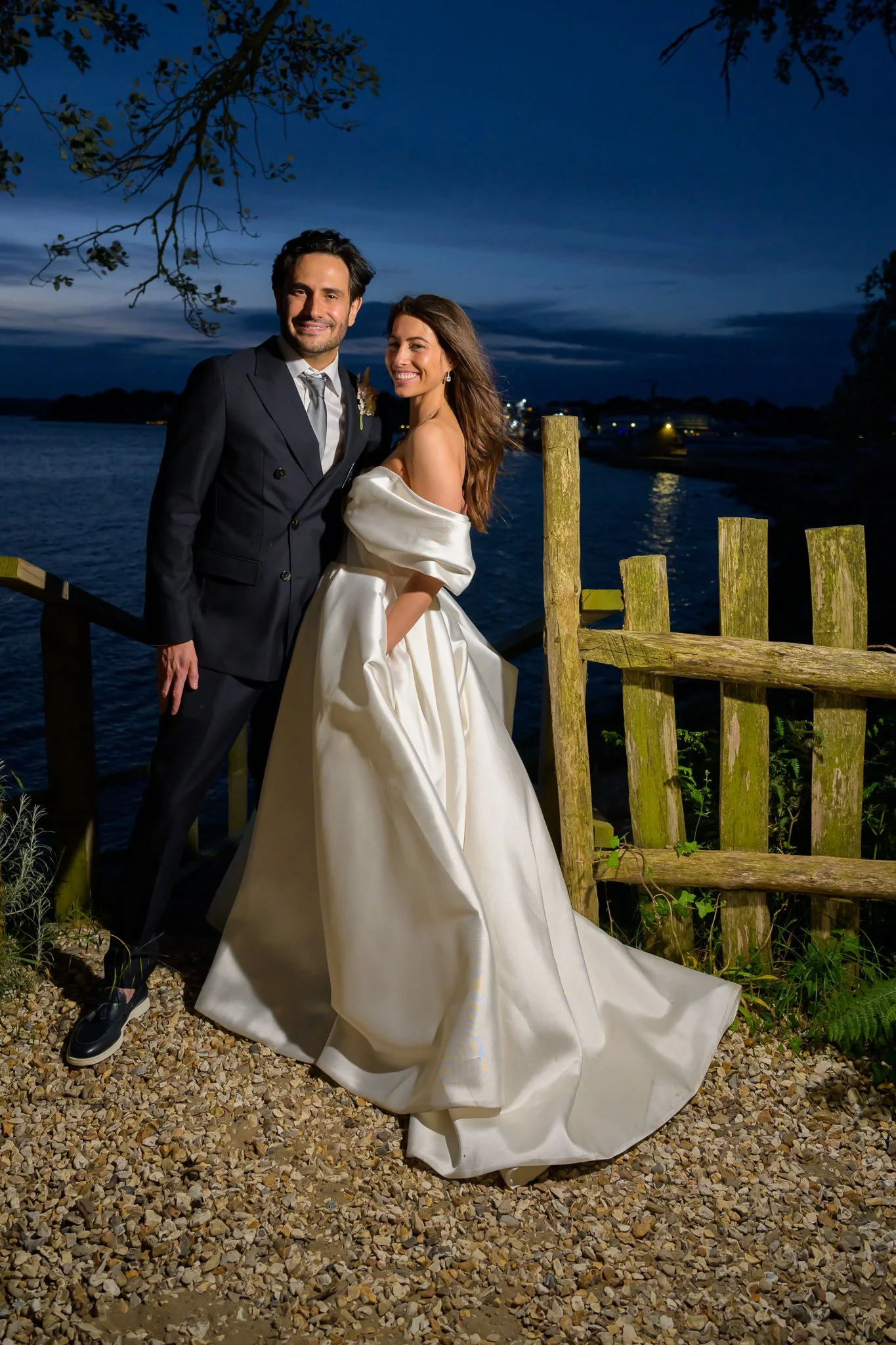 Bride and groom posing for a picture with a dark blue sky and fence in the background