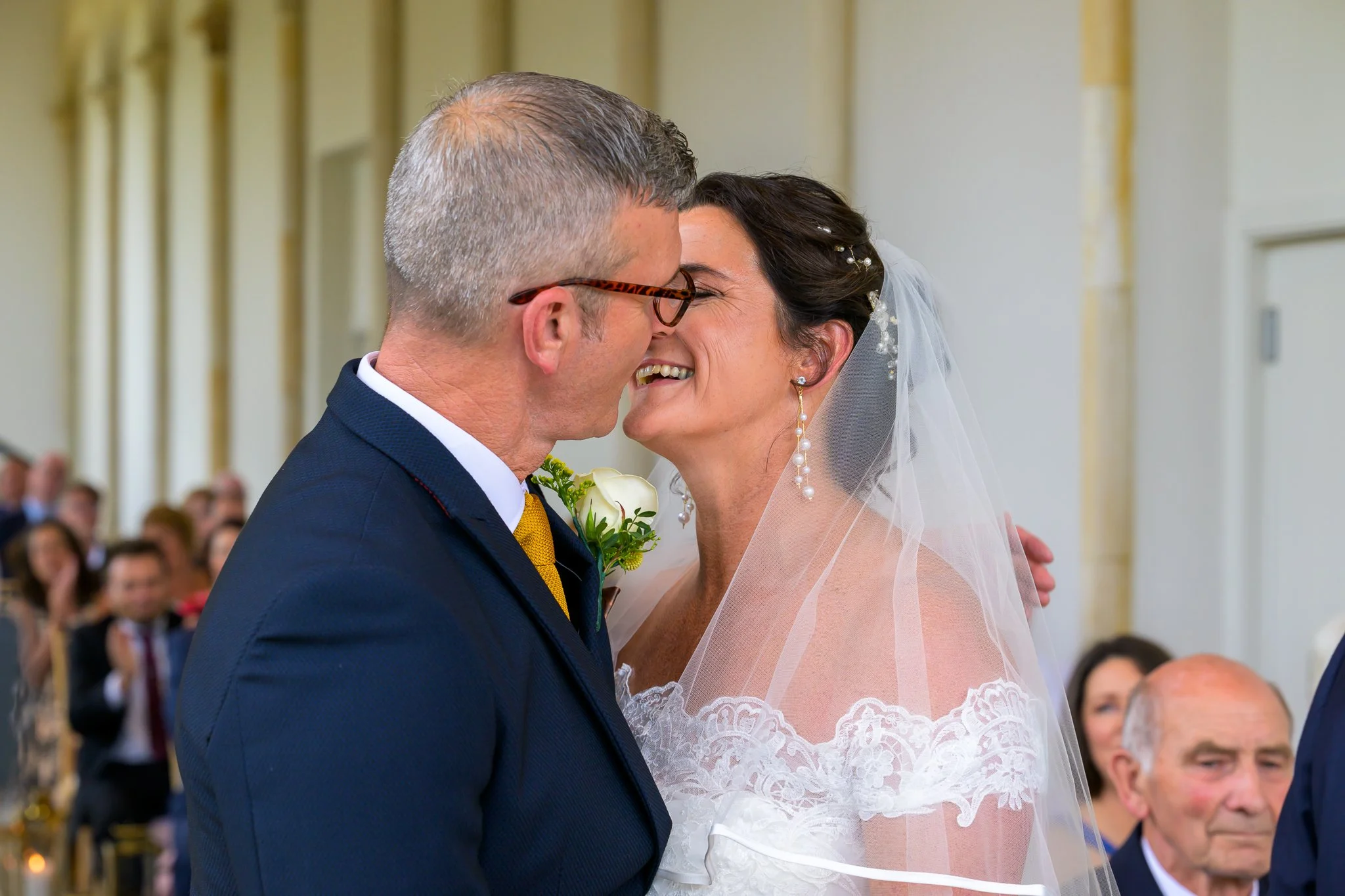 Bride and groom kissing and enjoying the moment at their wedding with their wedding guests in the background