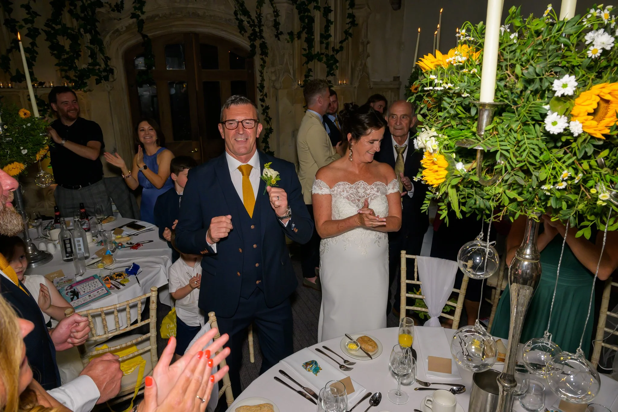 Bride and groom stood in the dining area of their wedding venue, with their guests surrounding them