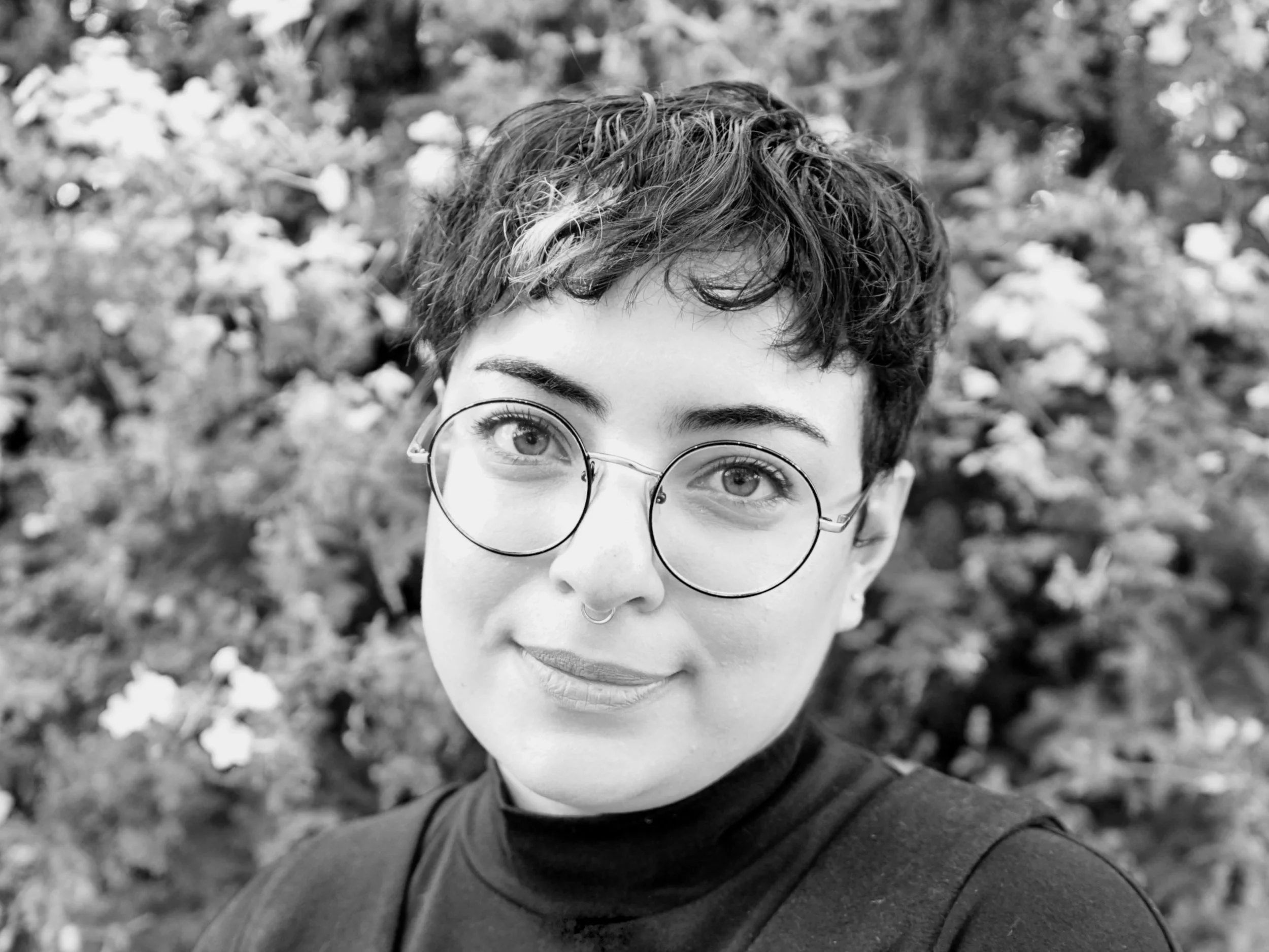 Black and white headshot of a woman/nonbinary person with a short haircut, glasses and a turtleneck.