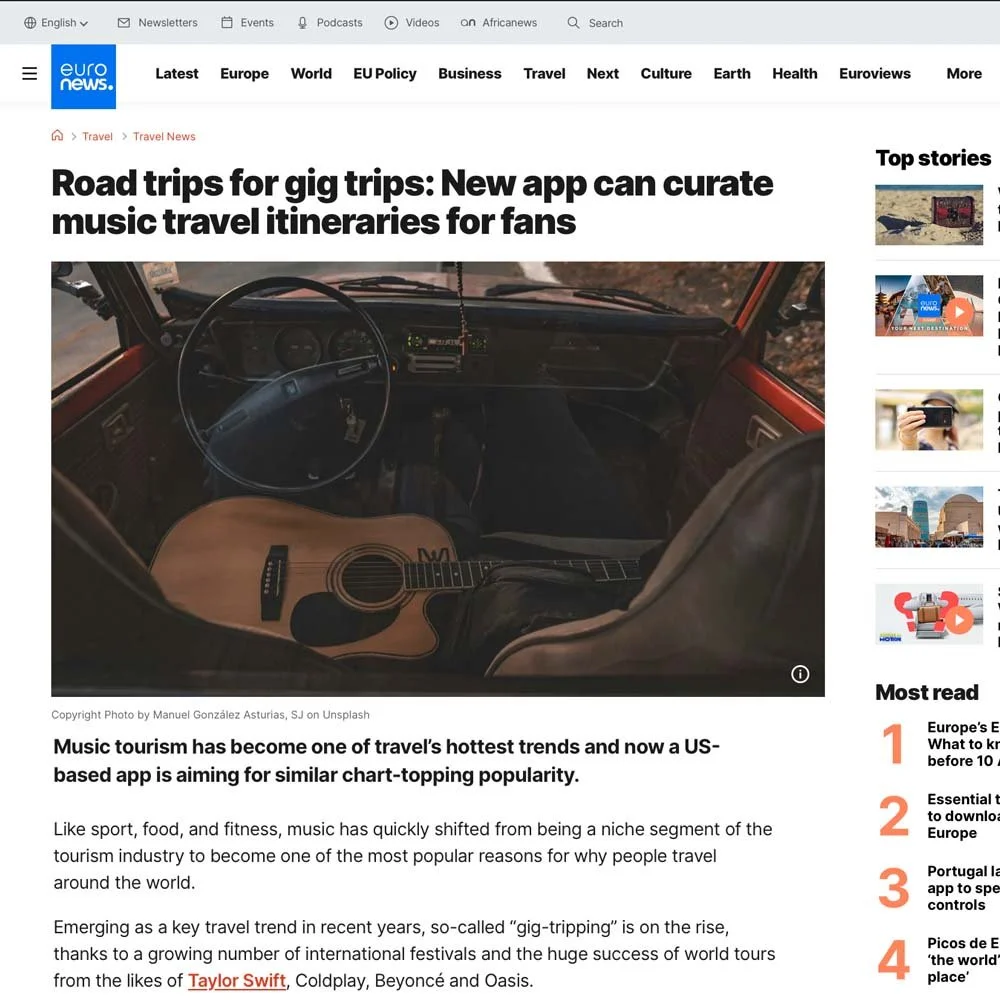 Photo of the inside of a vehicle with a steering wheel, dashboard, and an acoustic guitar laying on the passenger seat, taken from the back seat.