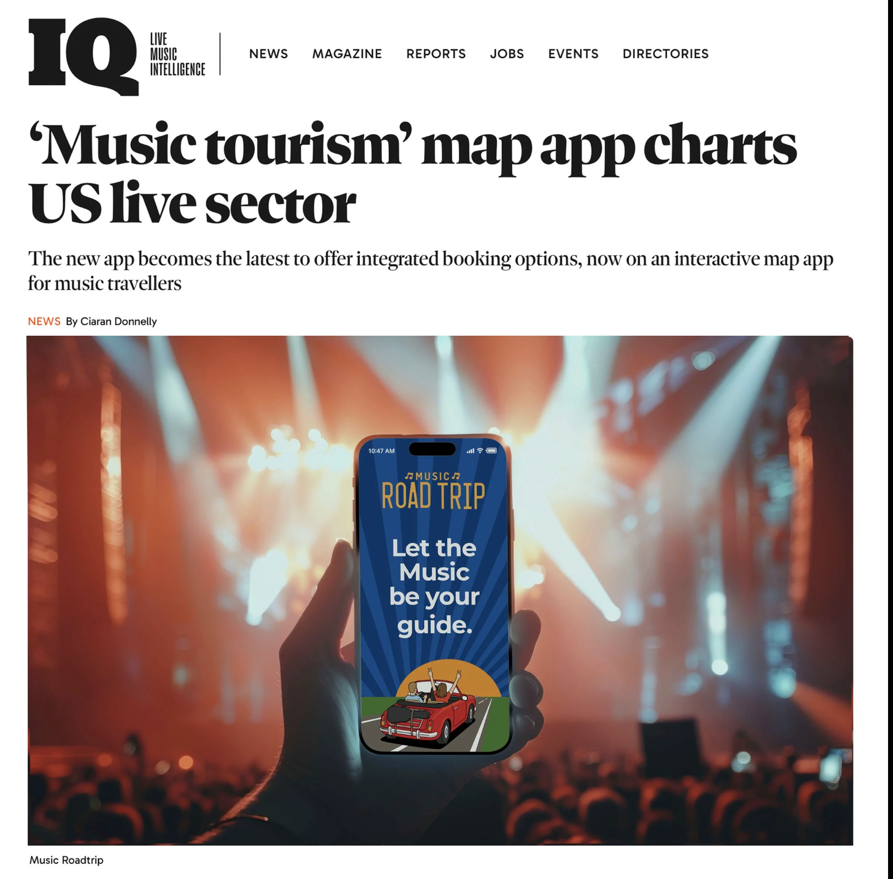 A person holding a smartphone with a music app on the screen that says "Music Road Trip" and "Let the Music be your guide" in front of a concert stage with bright lights and an audience.