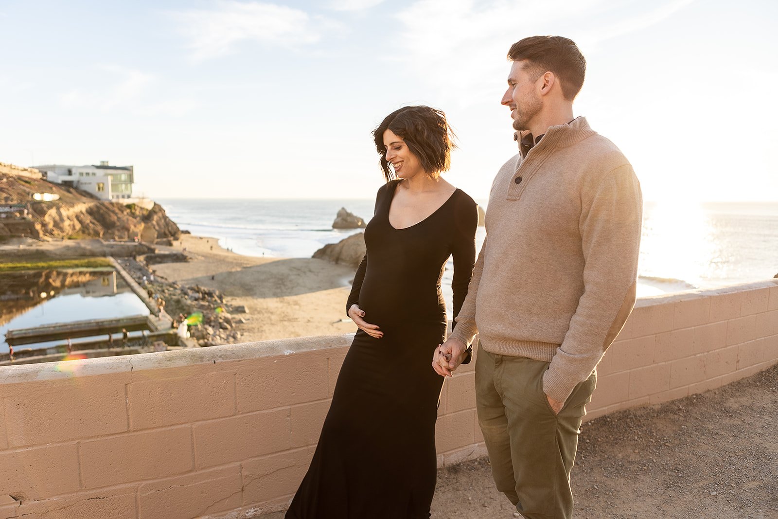 Expectant parents sharing a moment by the coastal cliffs overlooking the Sutro Baths during their San Francisco Bay Area maternity photo session, the ocean breeze enhancing the natural ambiance.