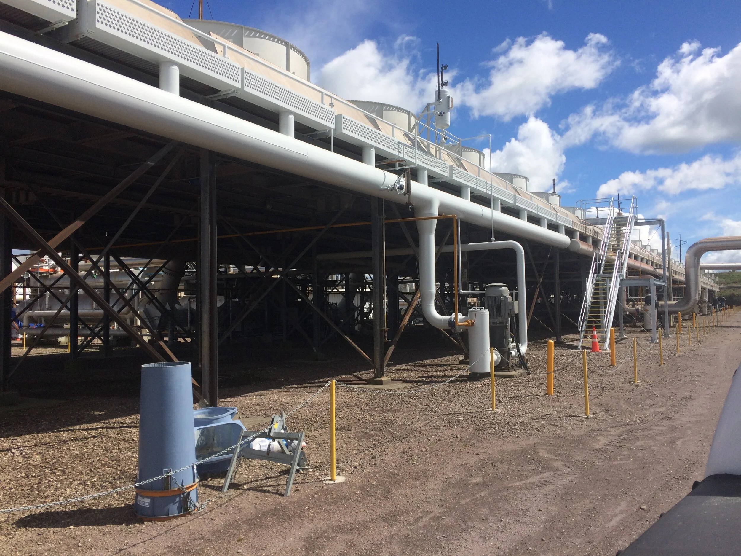 Industrial cooling system with pipes and large fans under a clear sky.