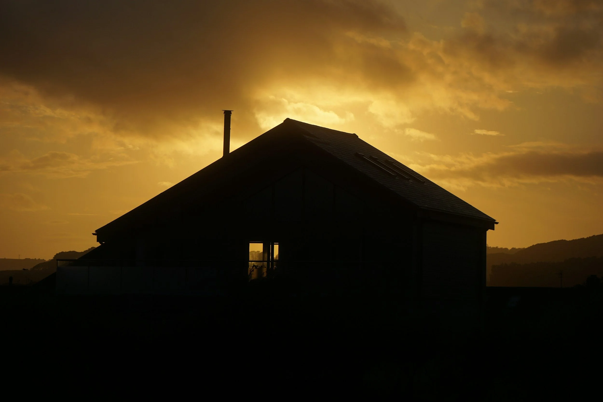 Dark shadow outline of a house in front of an orange and yellow cloudy sunset