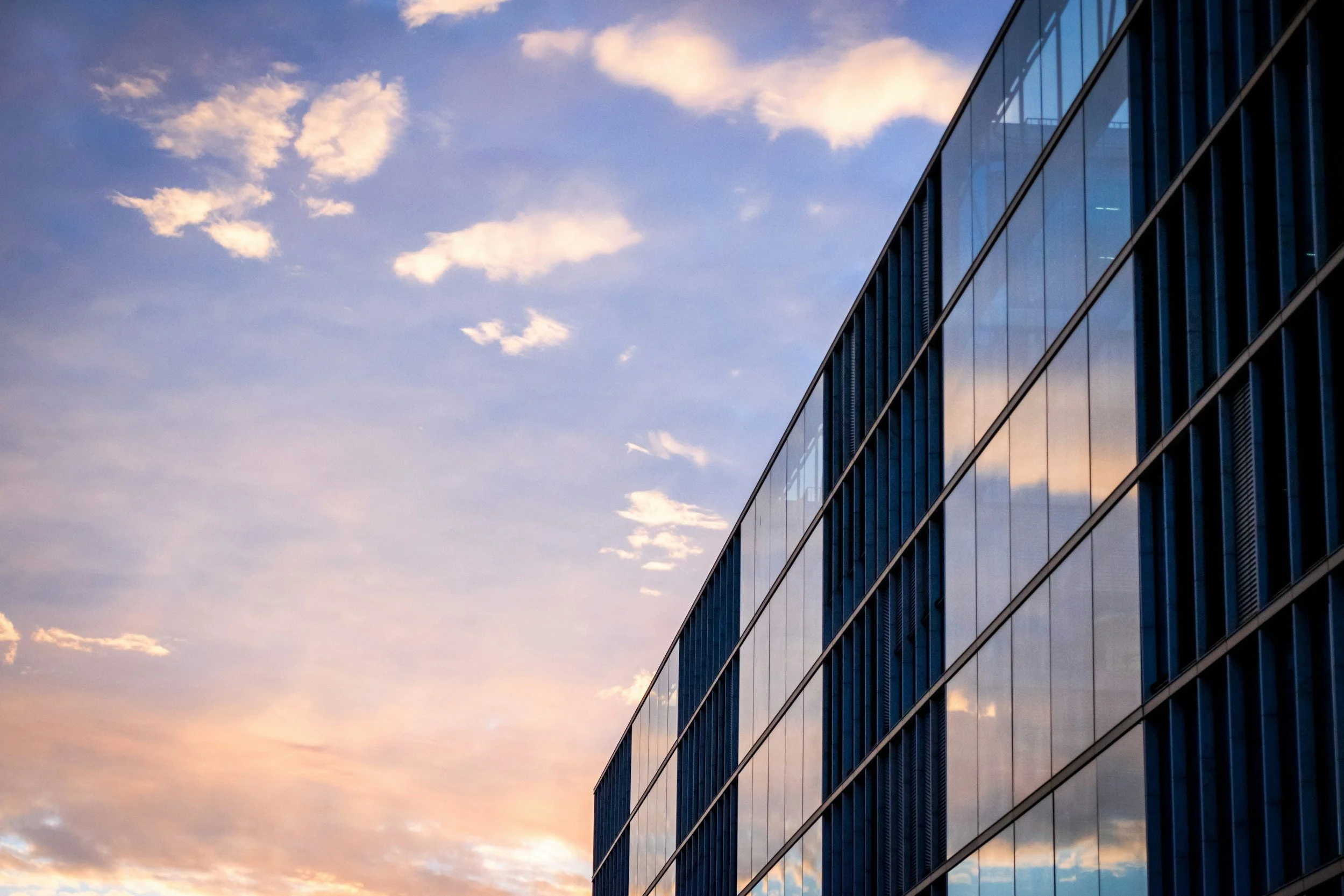 Corporate building with blue and purple sky fading into soft pink with cloud reflections on glass windows