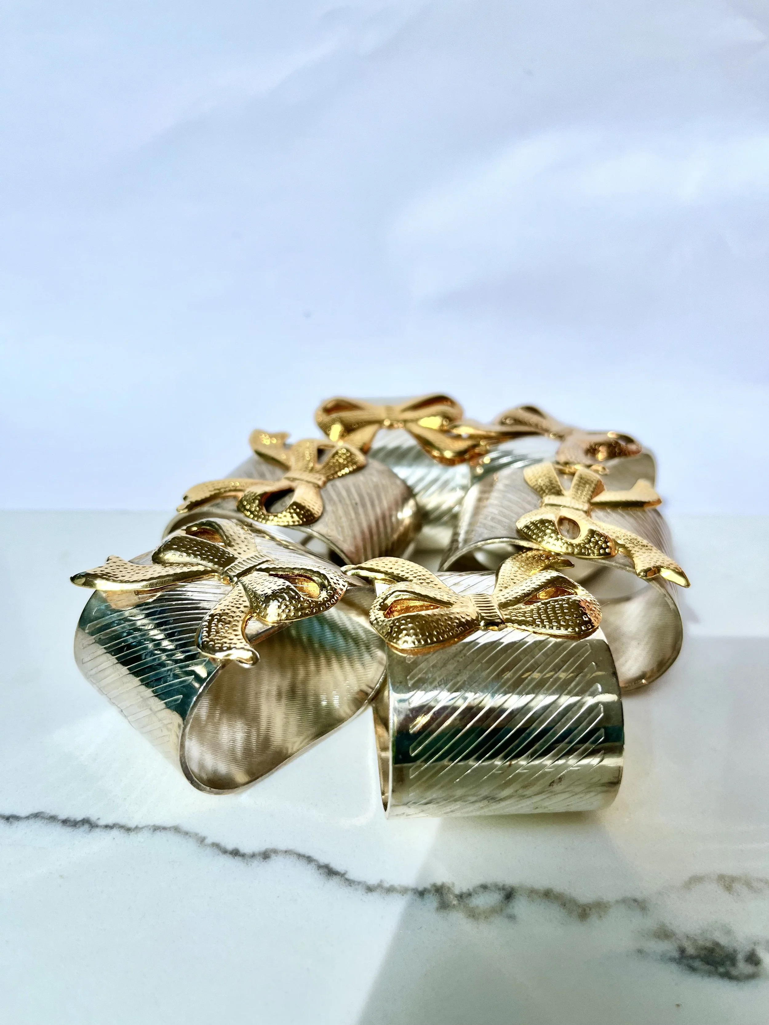 Close-up of a silver napkin holder with gold bow decorations on a white marble surface.
