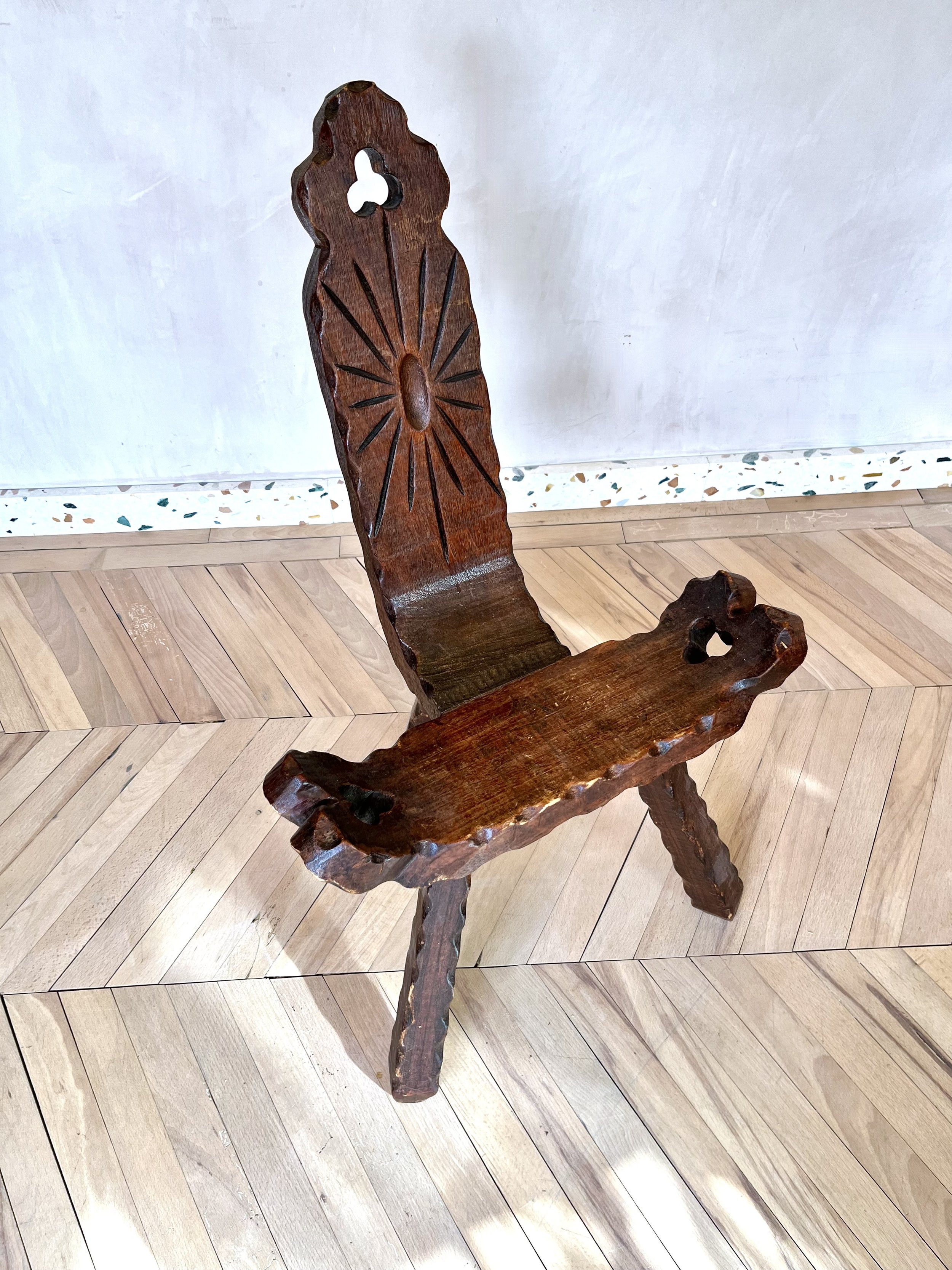 Wooden chair with carved scenery backrest, placed on wooden floor in front of a white wall.