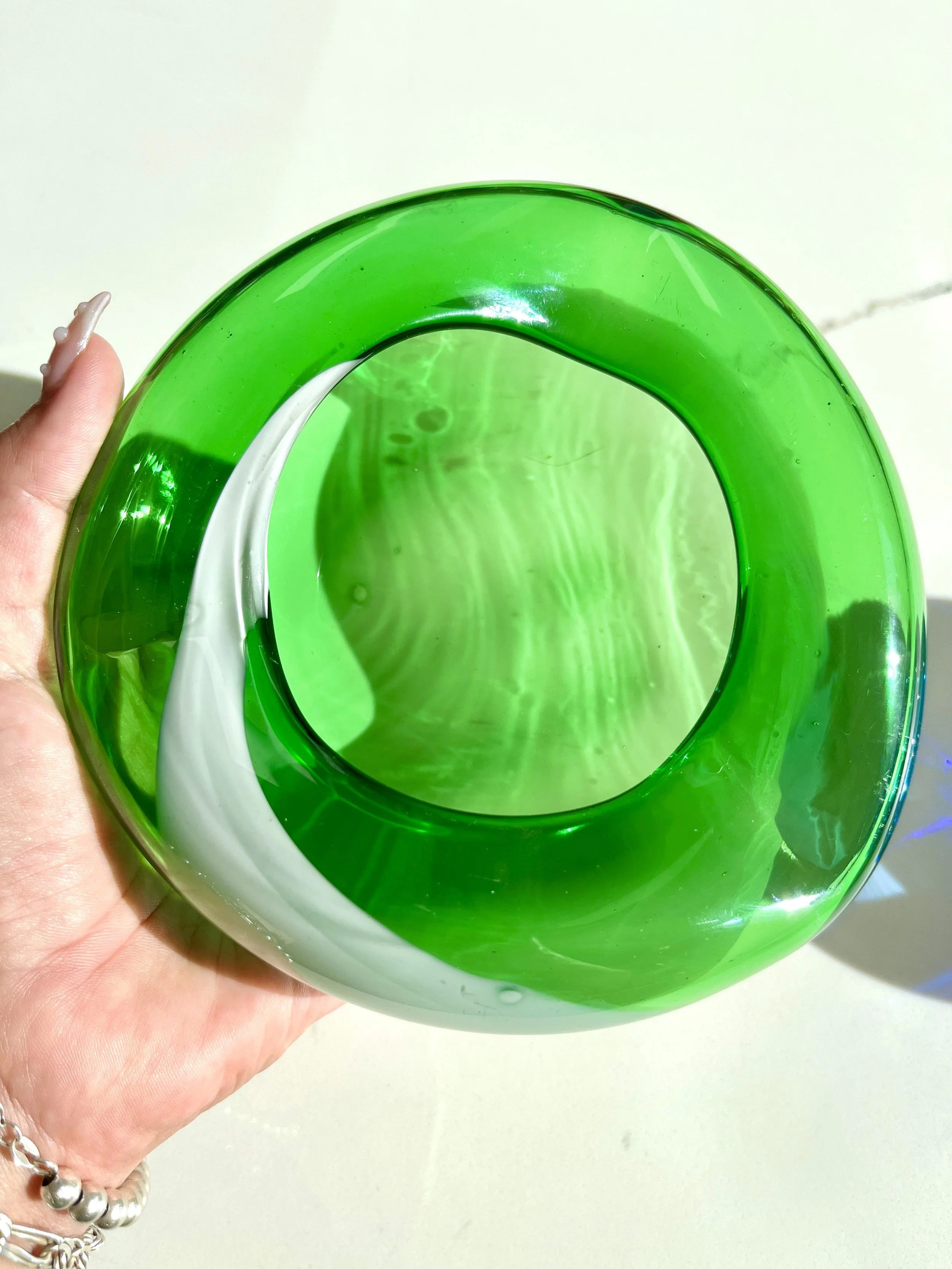 A hand holding a green glass bowl with a white interior, showing reflections and shadows of the person and surroundings.