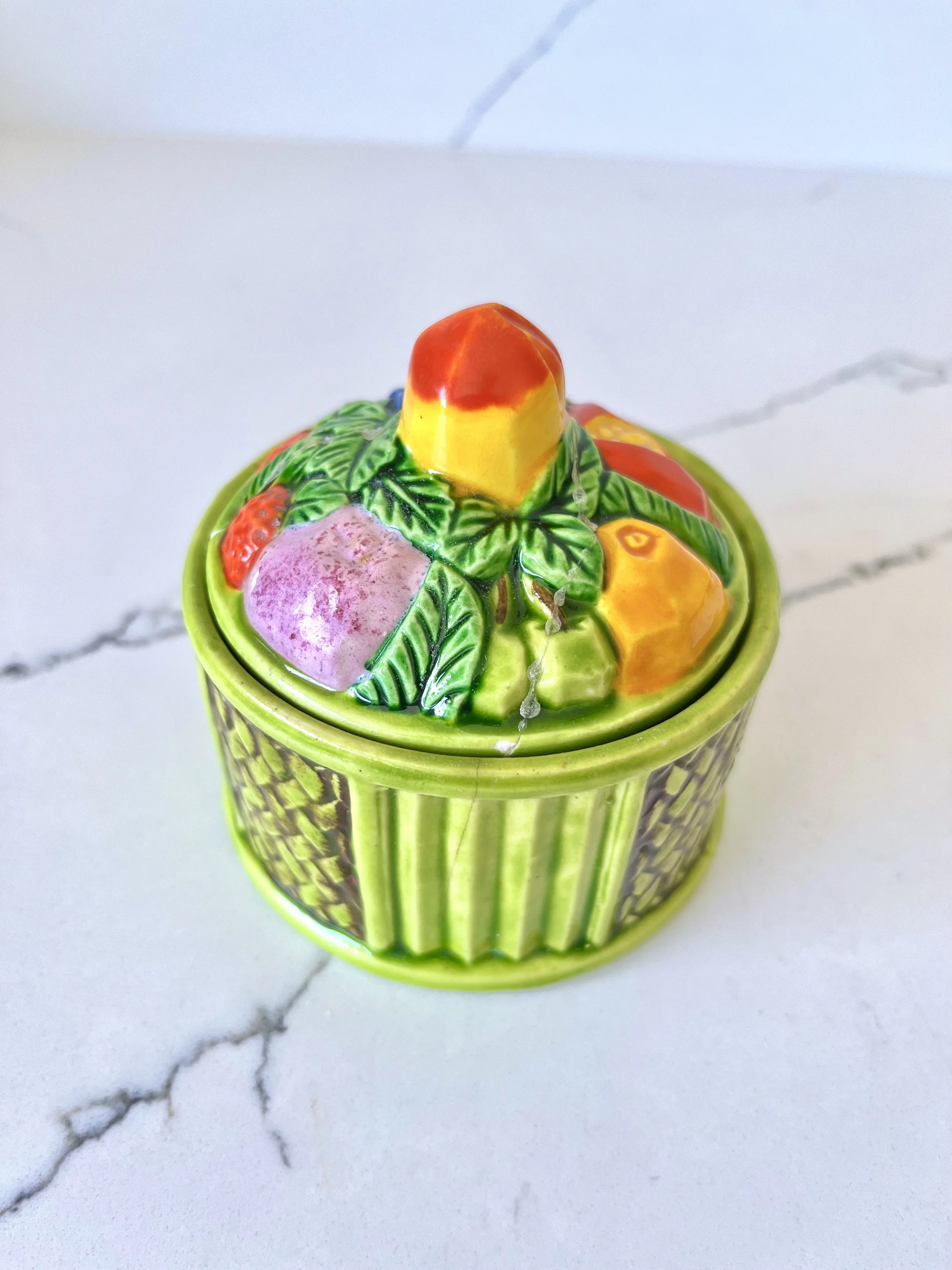 Colorful ceramic container with tropical fruit and leaves design, on a white marble surface.