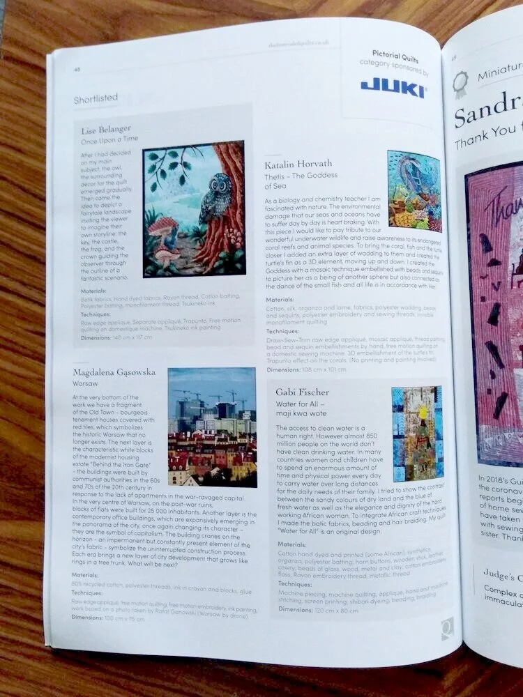 Open book showing pages with descriptions and images of quilt art, including a colorful quilt depicting an owl in a tree, and a cityscape quilt of Warsaw, with text about various artists and their work.