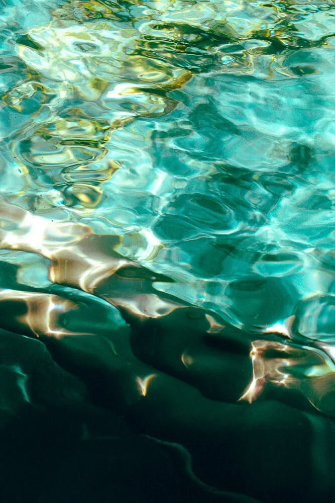 Close-up of clear, rippling water with sunlight reflections creating colorful patterns.