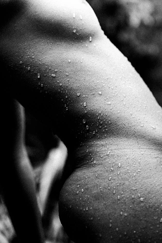 Close-up of a human torso with water droplets on the skin, shown in black and white.