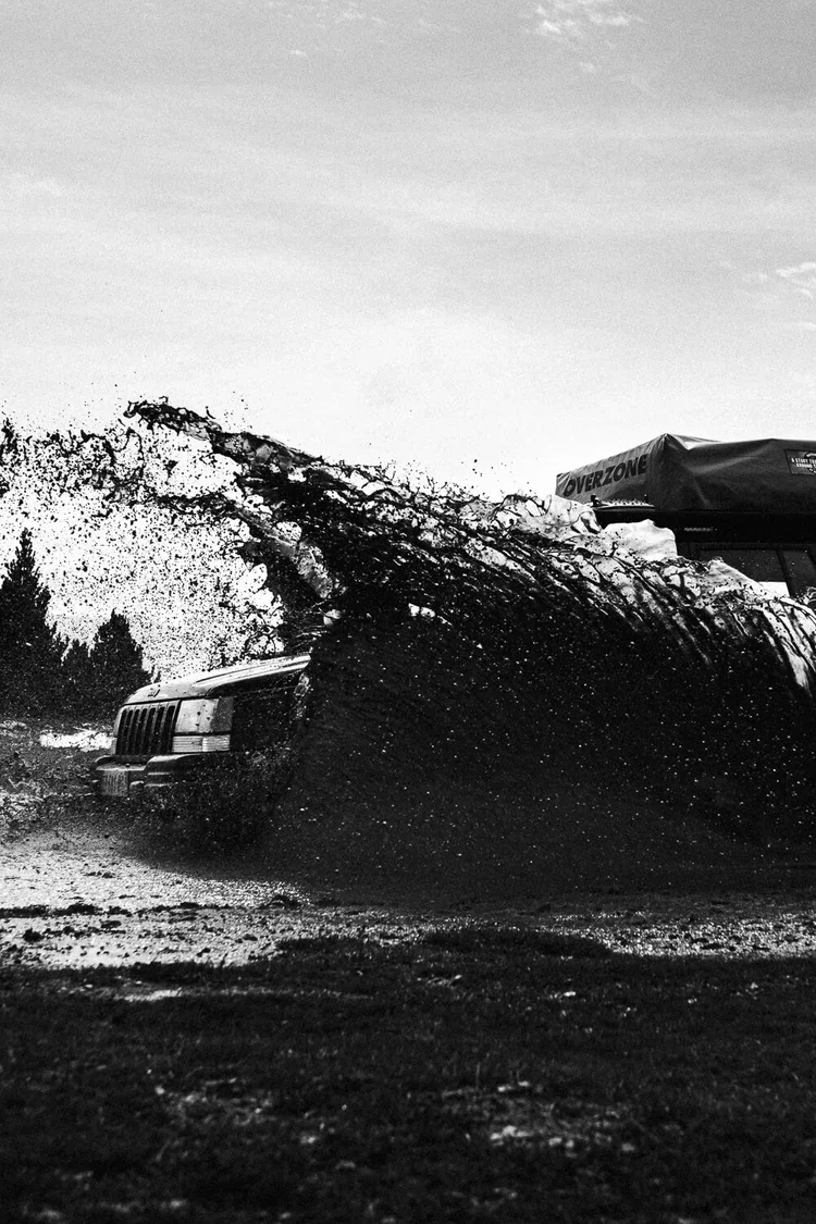 Un véhicule roulant à grande vitesse dans l'eau, créant une éclaboussure massive sur fond de ciel nuageux.