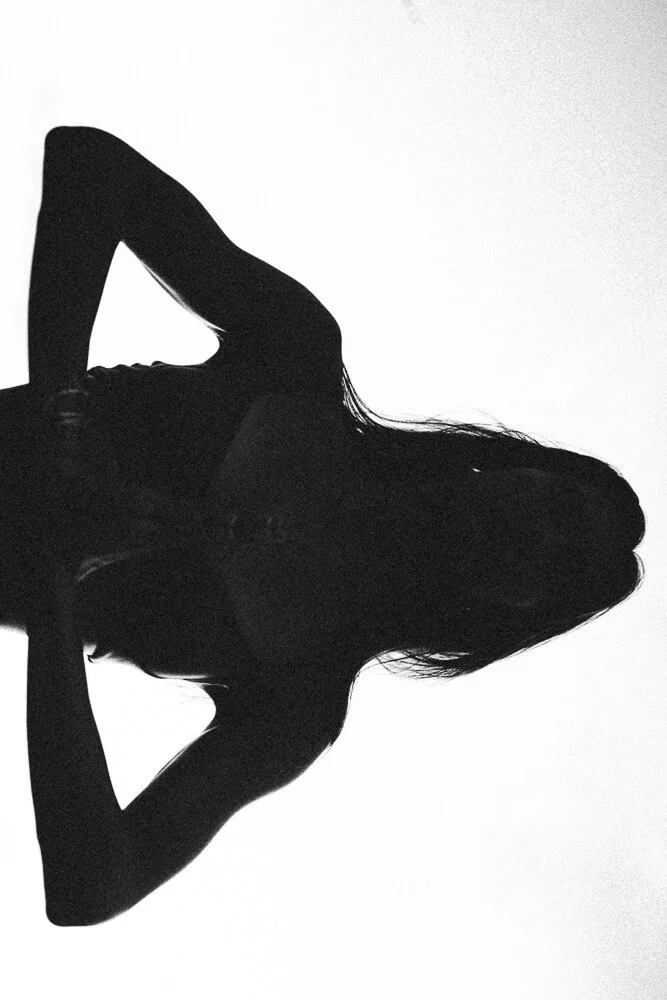 Silhouette of a woman with long hair, arms raised with hands behind her head, against a white background.