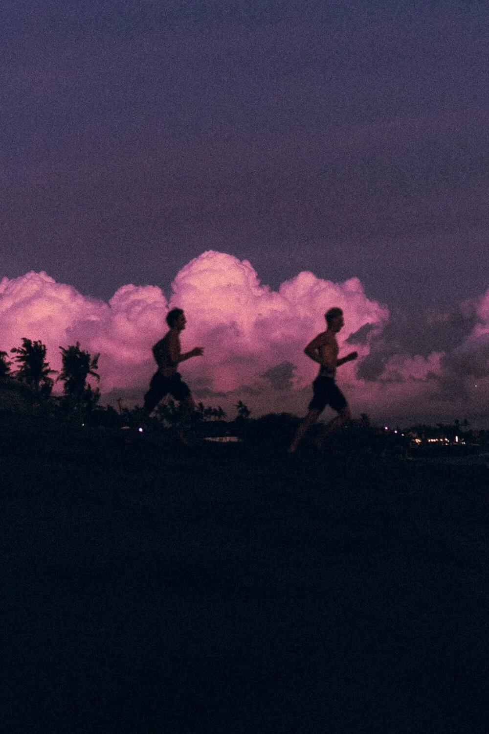 Deux personnes courent le long d'une plage au crépuscule, avec un ciel violet et des nuages roses en arrière-plan.
