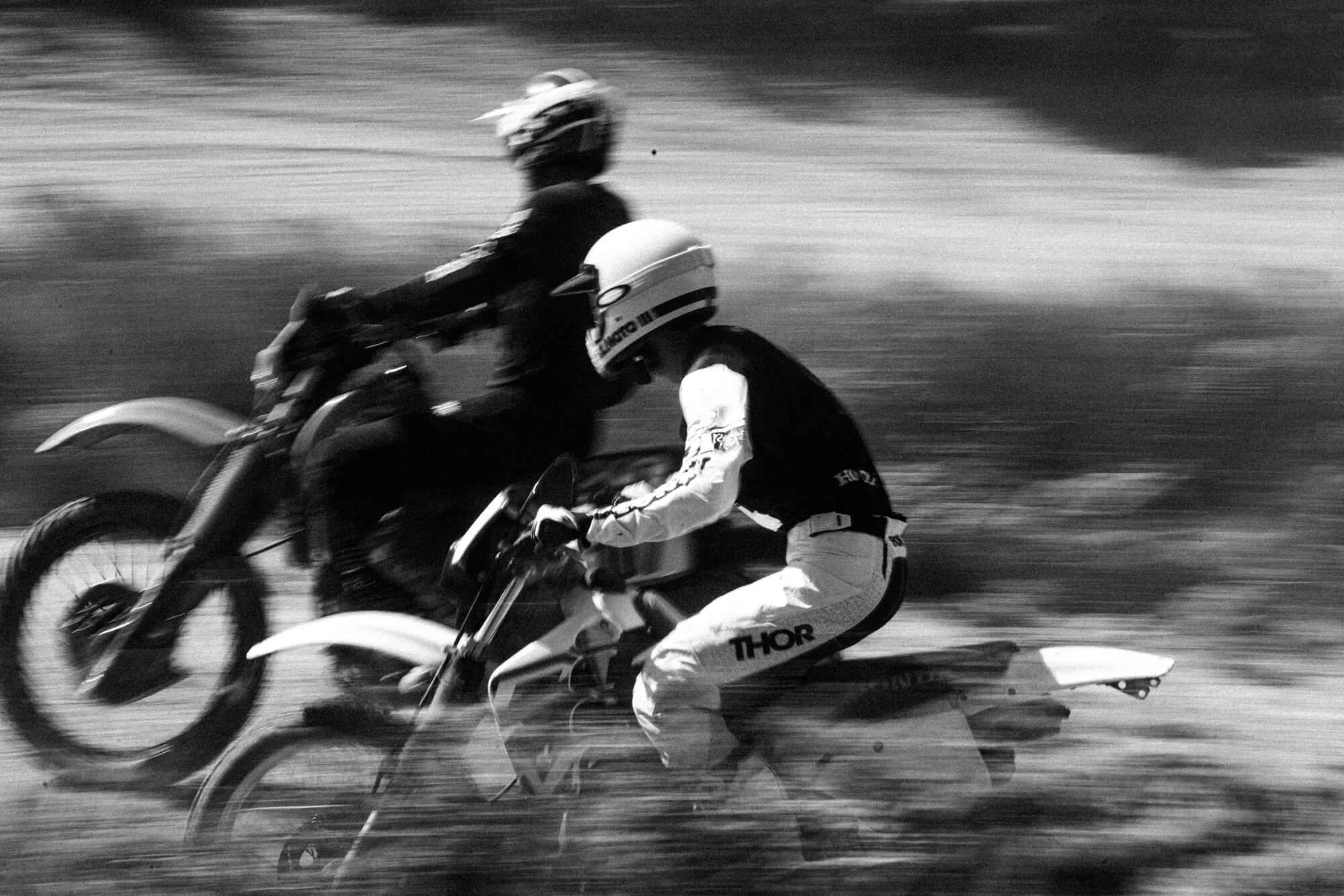 Black and white photo of a motocross rider on a dirt bike in motion, with a blurred background emphasizing speed and movement.