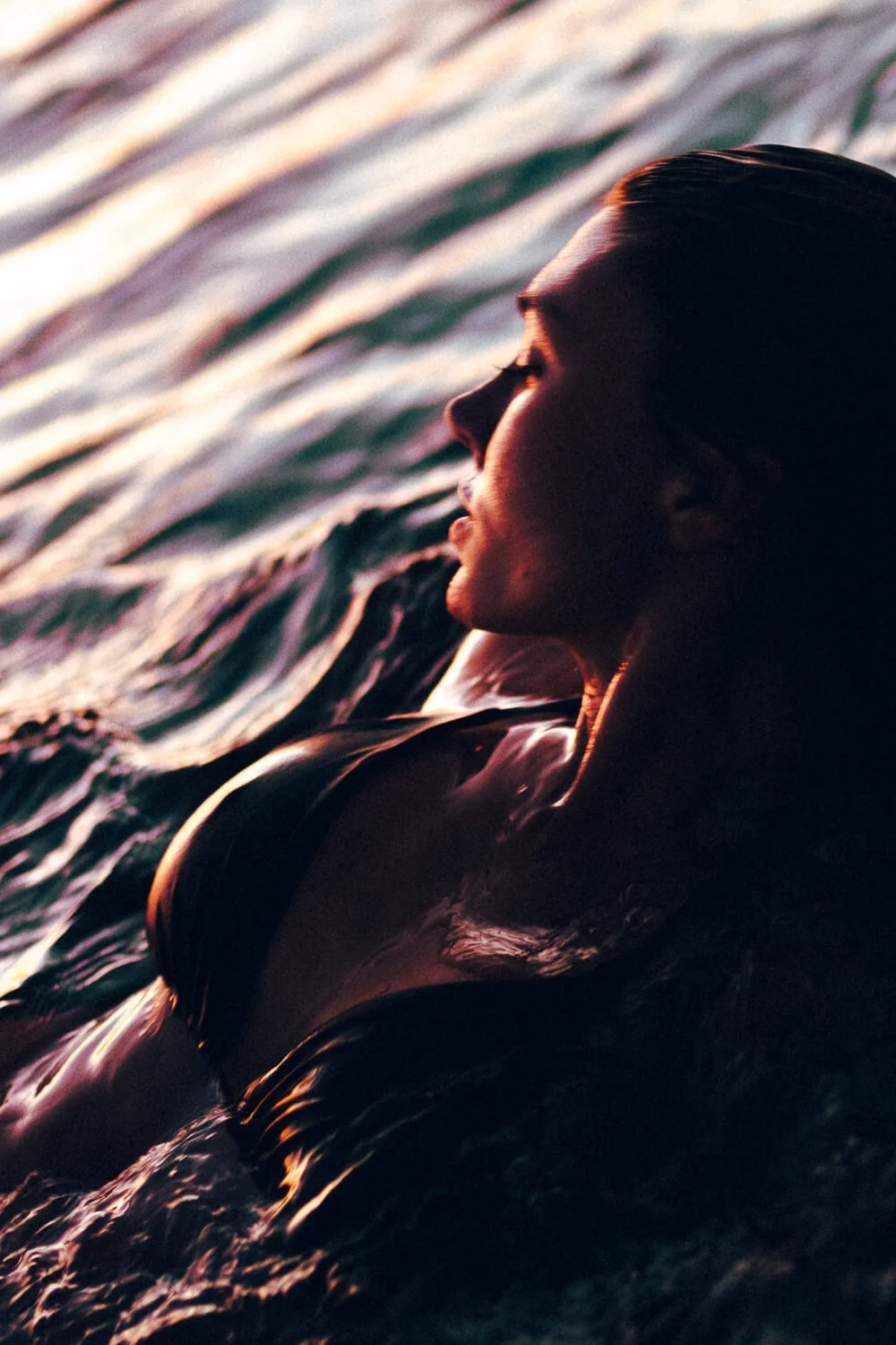 Femme dans l'eau au coucher du soleil, profil, ambiance douce et lumineuse.