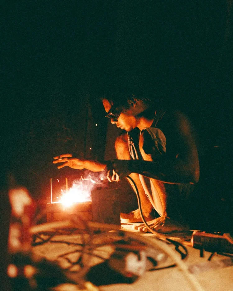 Une personne portant des lunettes travaille sur un projet en utilisant une source de chaleur dans un environnement sombre.