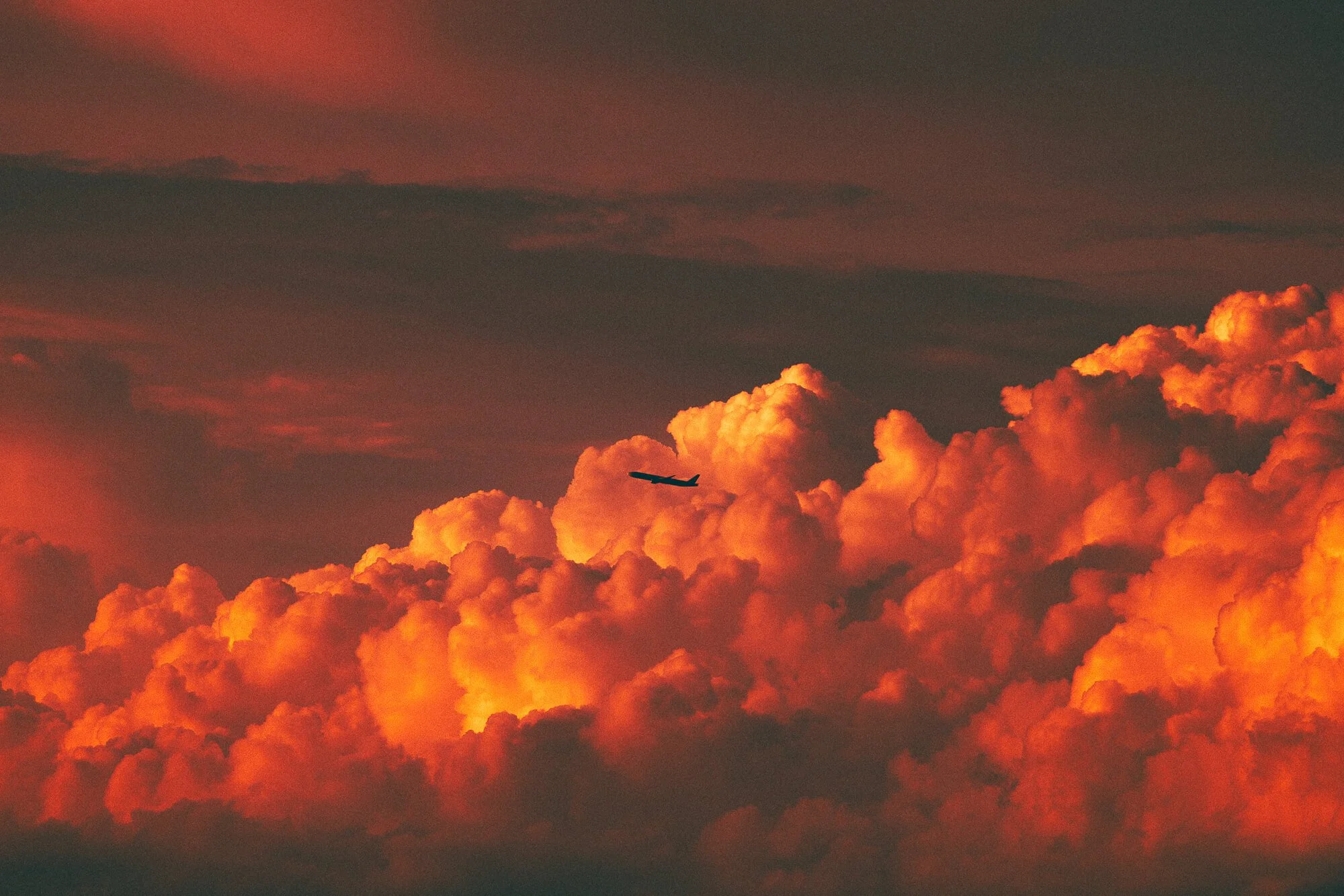 Un avion survole des nuages orange et rouges lors d'un coucher de soleil.