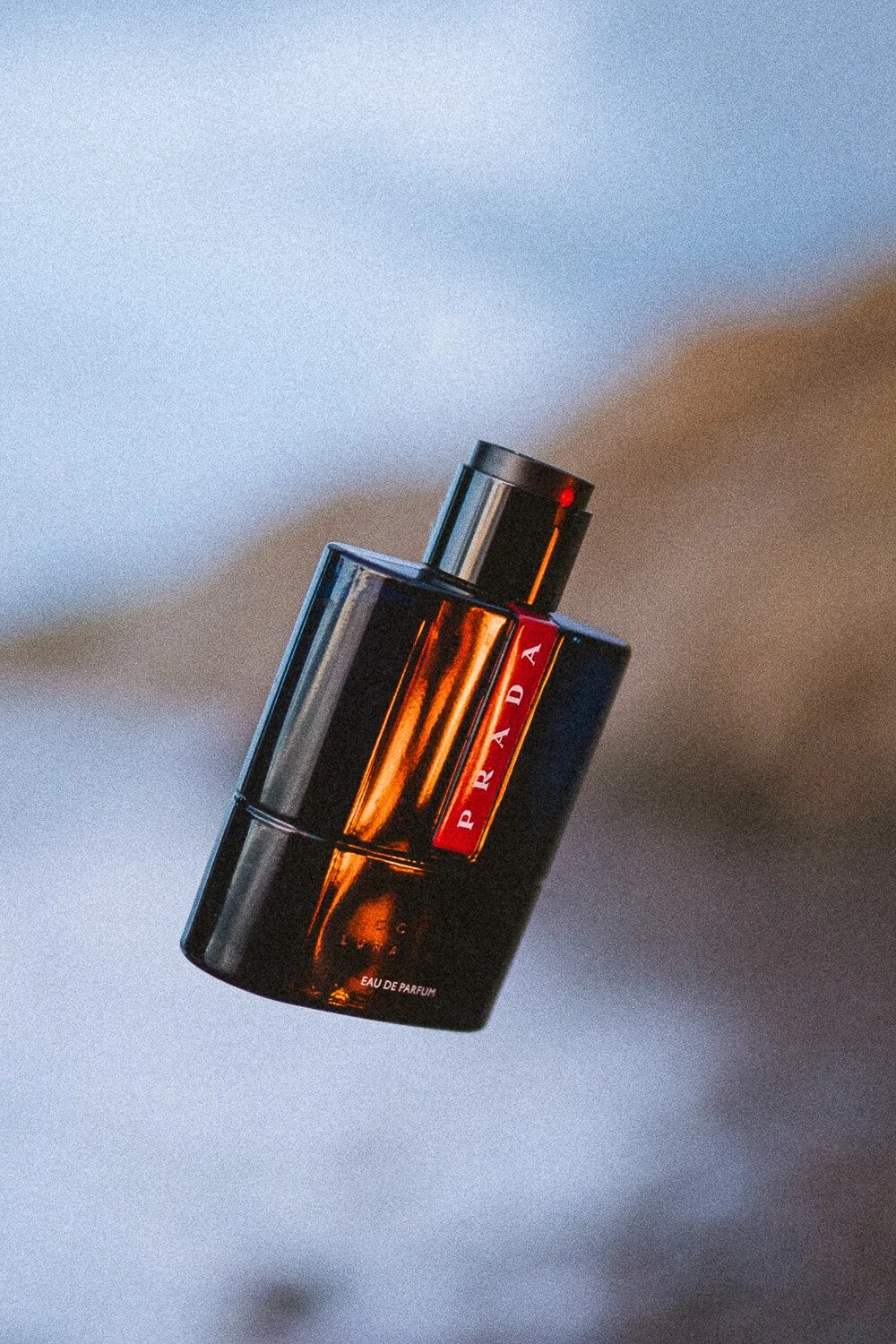 A bottle of Prada Eau de Parfum perfume with a black and amber design, floating in the air.