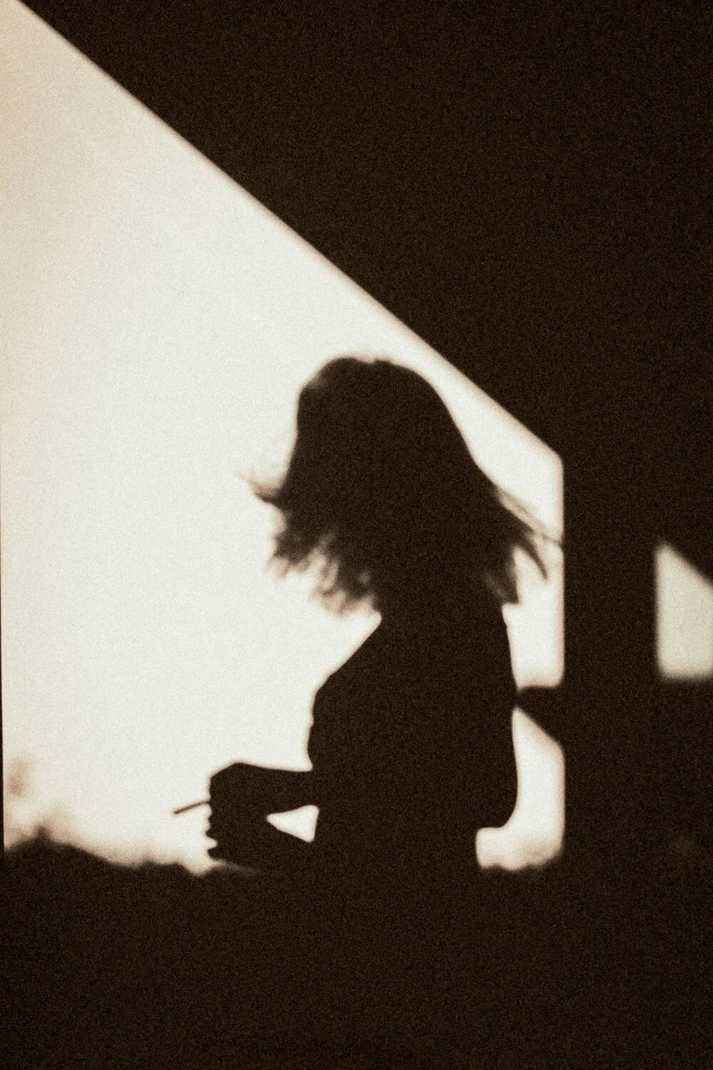 Silhouette of a woman with shoulder-length hair holding a cigarette, standing outdoors with a sunset or sunrise background.