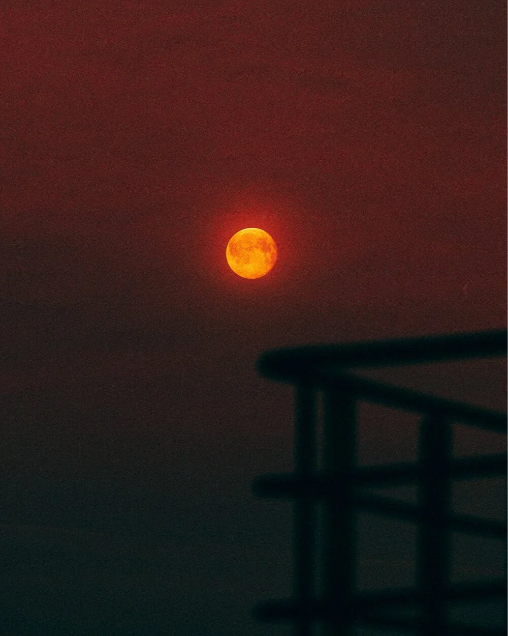 Une lune orange visible dans un ciel sombre, avec un bâtiment en silhouette au premier plan.