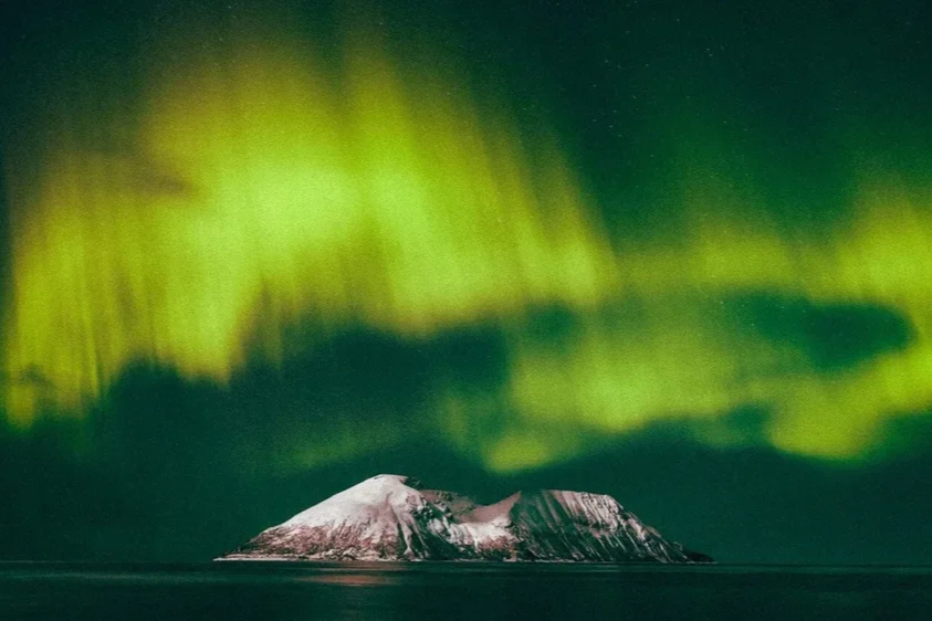 Aurores boréales vertes illuminant le ciel au-dessus d'une île couverte de neige.