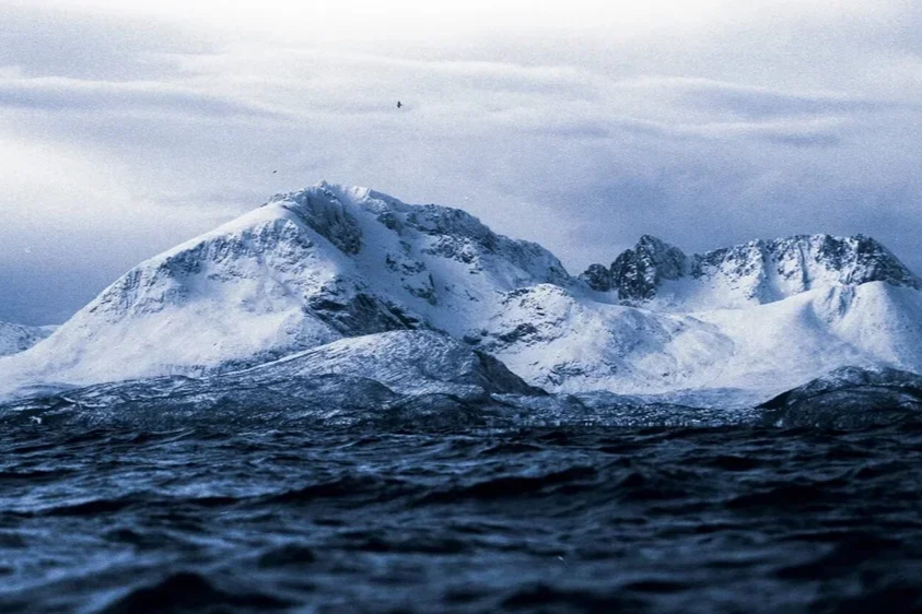 Montagne enneigée au bord de la mer, ciel nuageux.