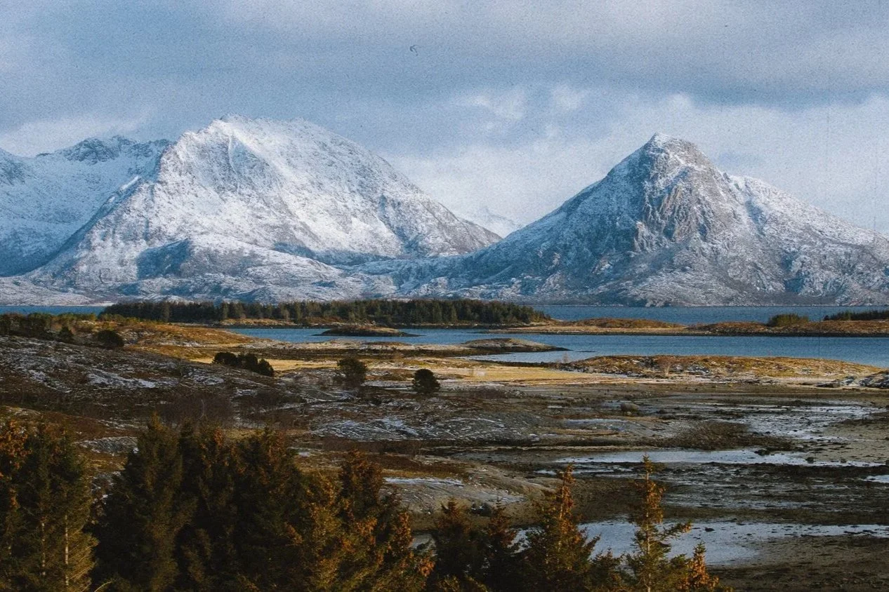 Montagnes enneigées avec un lac et une forêt au premier plan dans un paysage de Norvège.